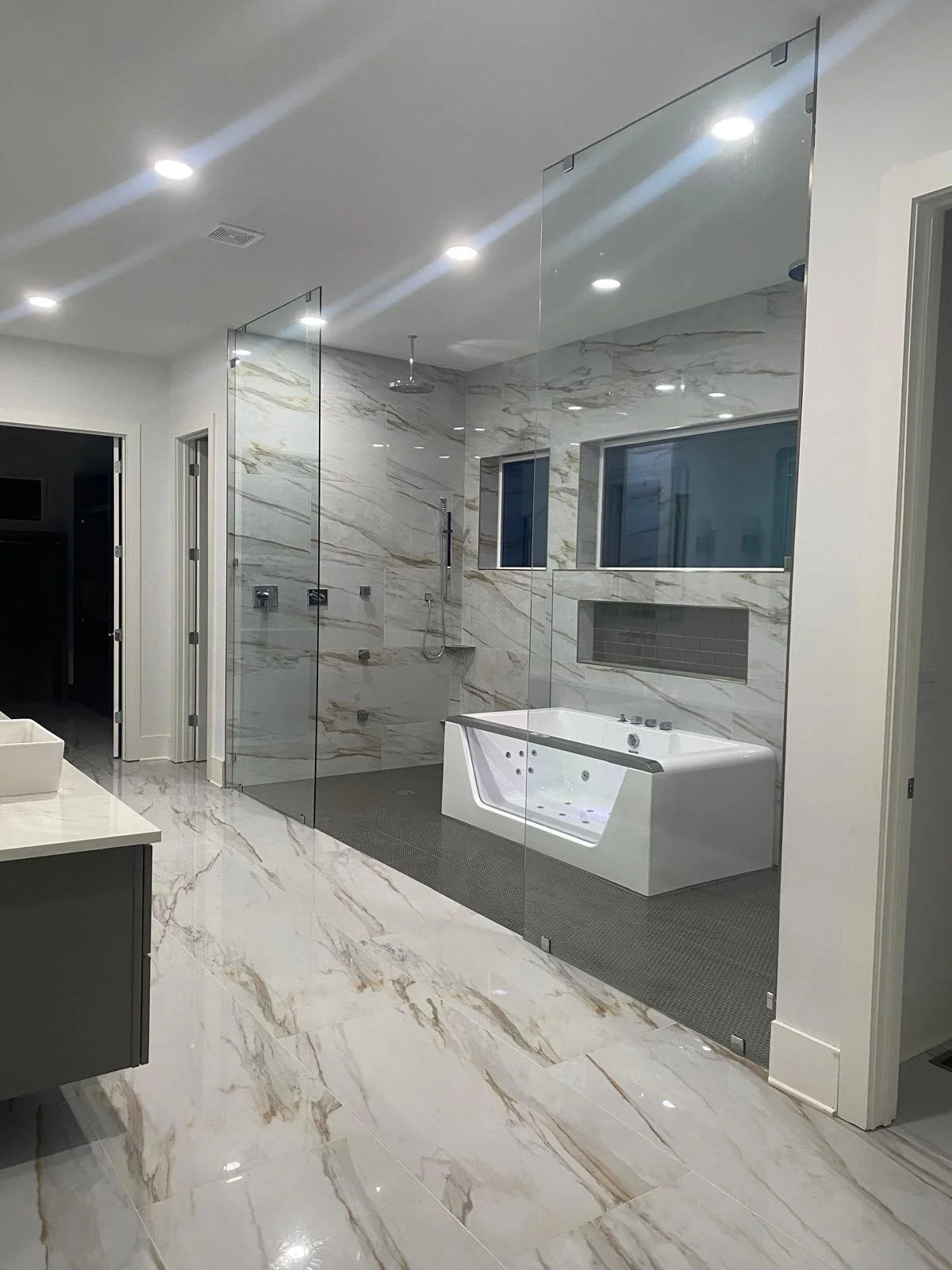 Modern bathroom with marble floors and walls, glass shower enclosure, built-in bathtub, and recessed lighting.