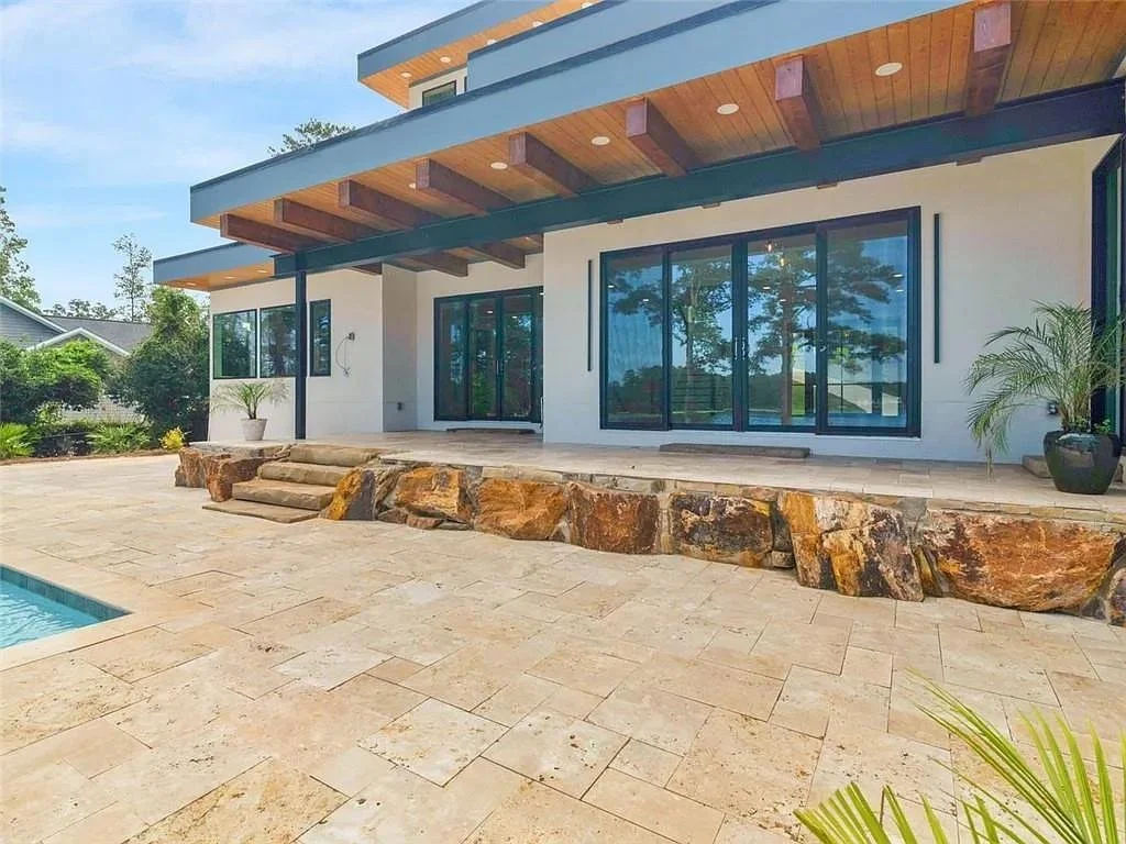 Modern house with large glass sliding doors, a stone patio, and a small pool in the backyard. There are potted plants and steps made of rocks leading up to the patio.