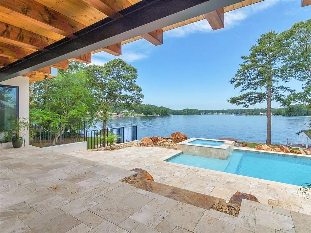View from a covered patio with a hot tub overlooking a river, trees, and a clear blue sky.