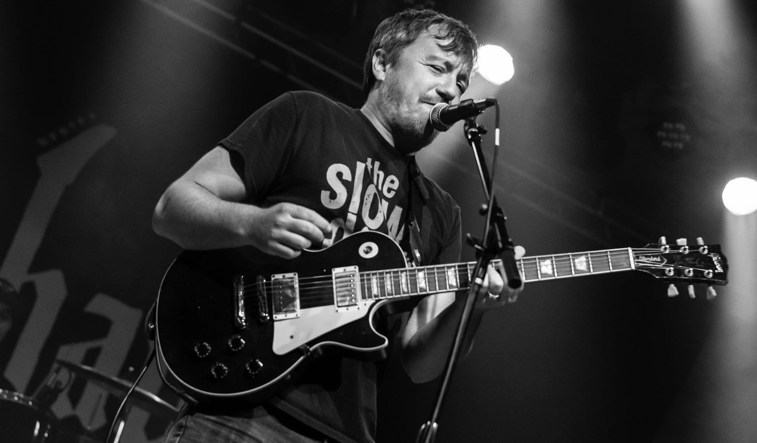 A man playing an electric guitar and singing into a microphone during a live music performance.