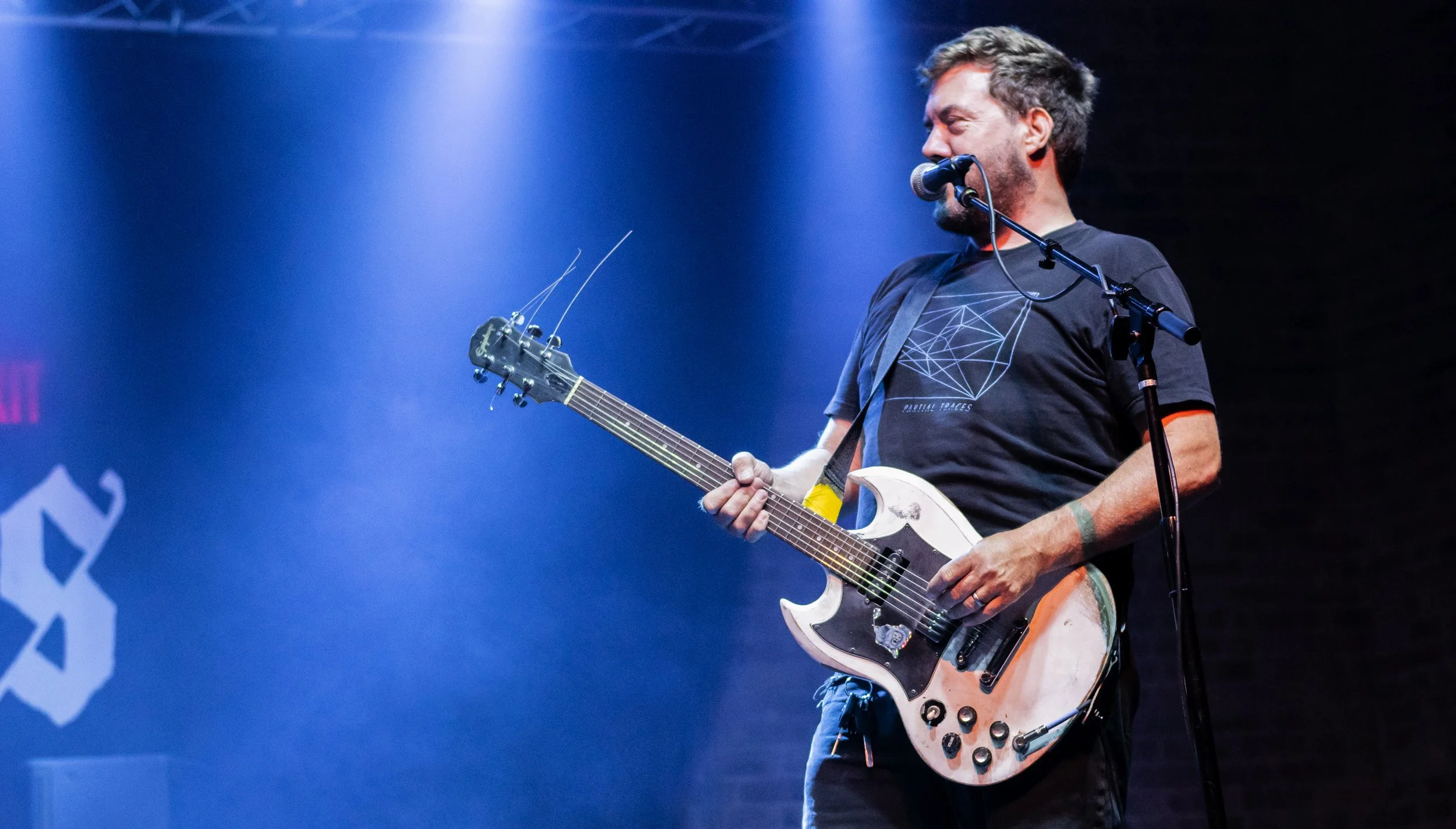 A man performing on stage, singing into a microphone and playing an electric guitar.