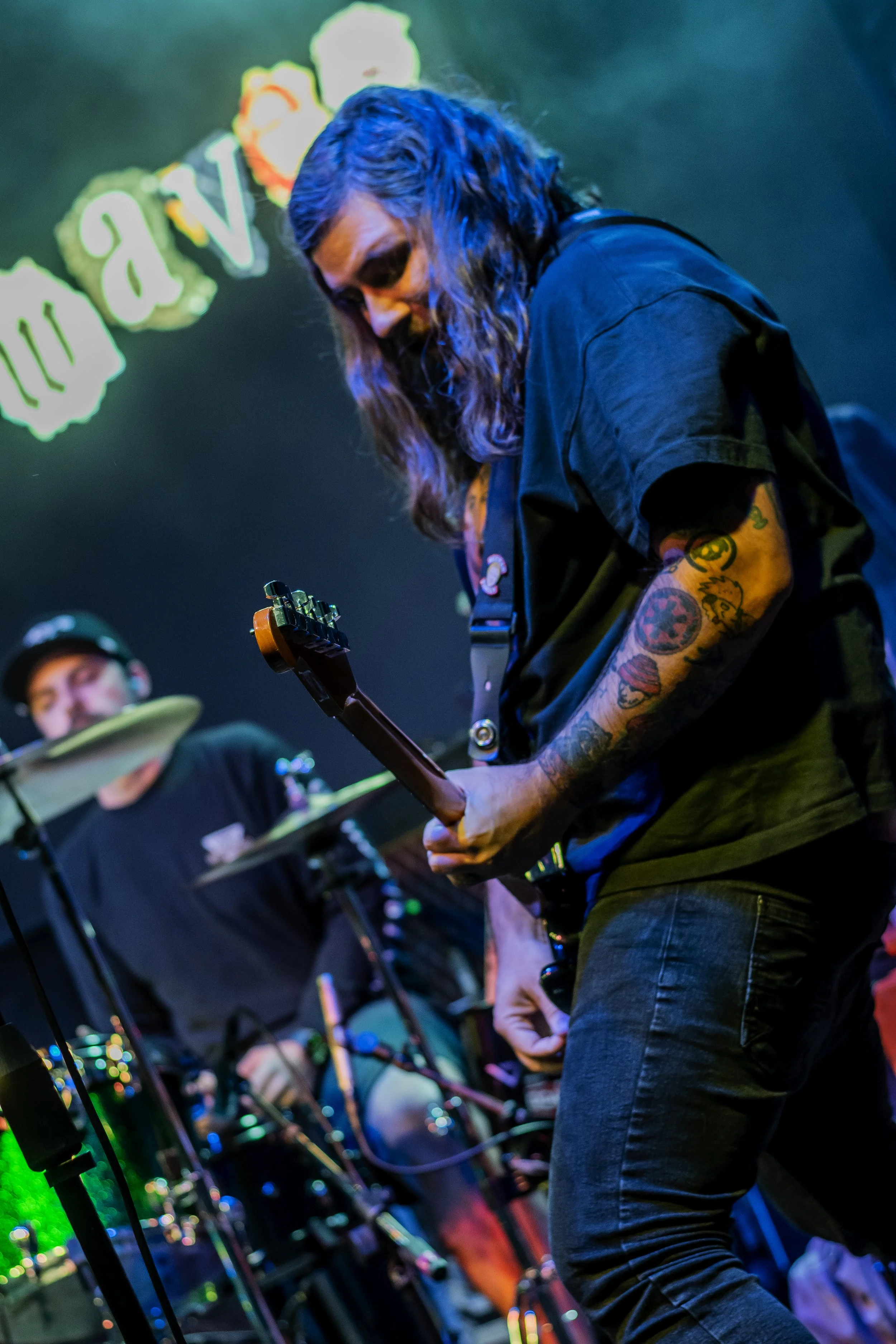 Musician playing electric guitar on stage with colorful background lights and a microphone stand.