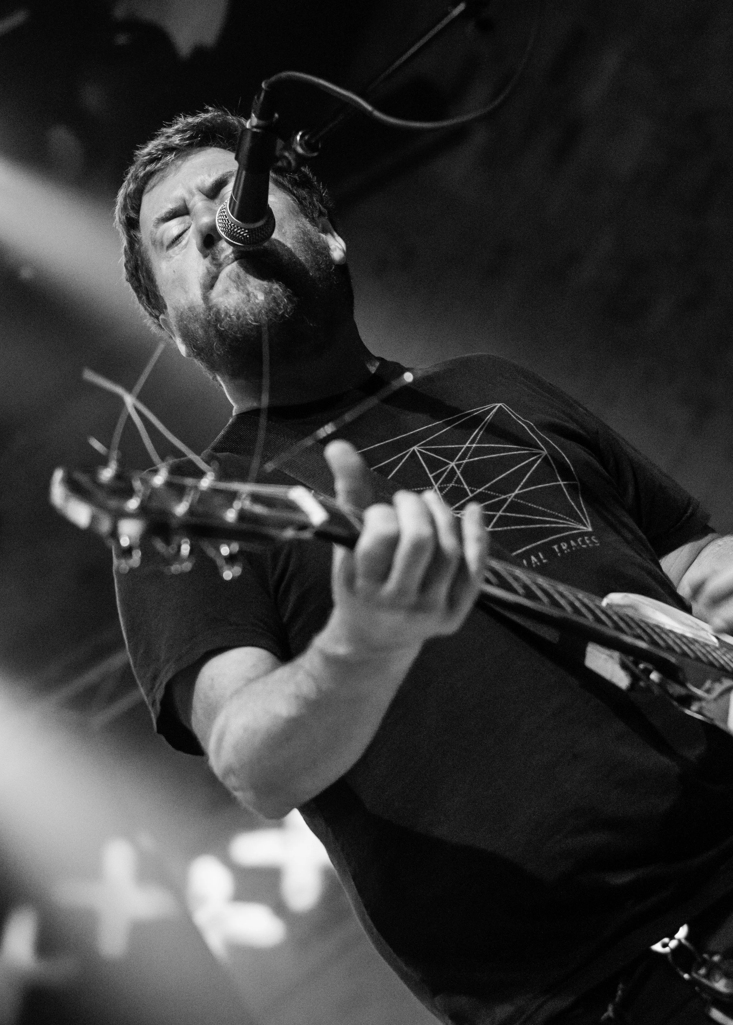 A man singing into a microphone while playing an electric guitar in a black and white photo.