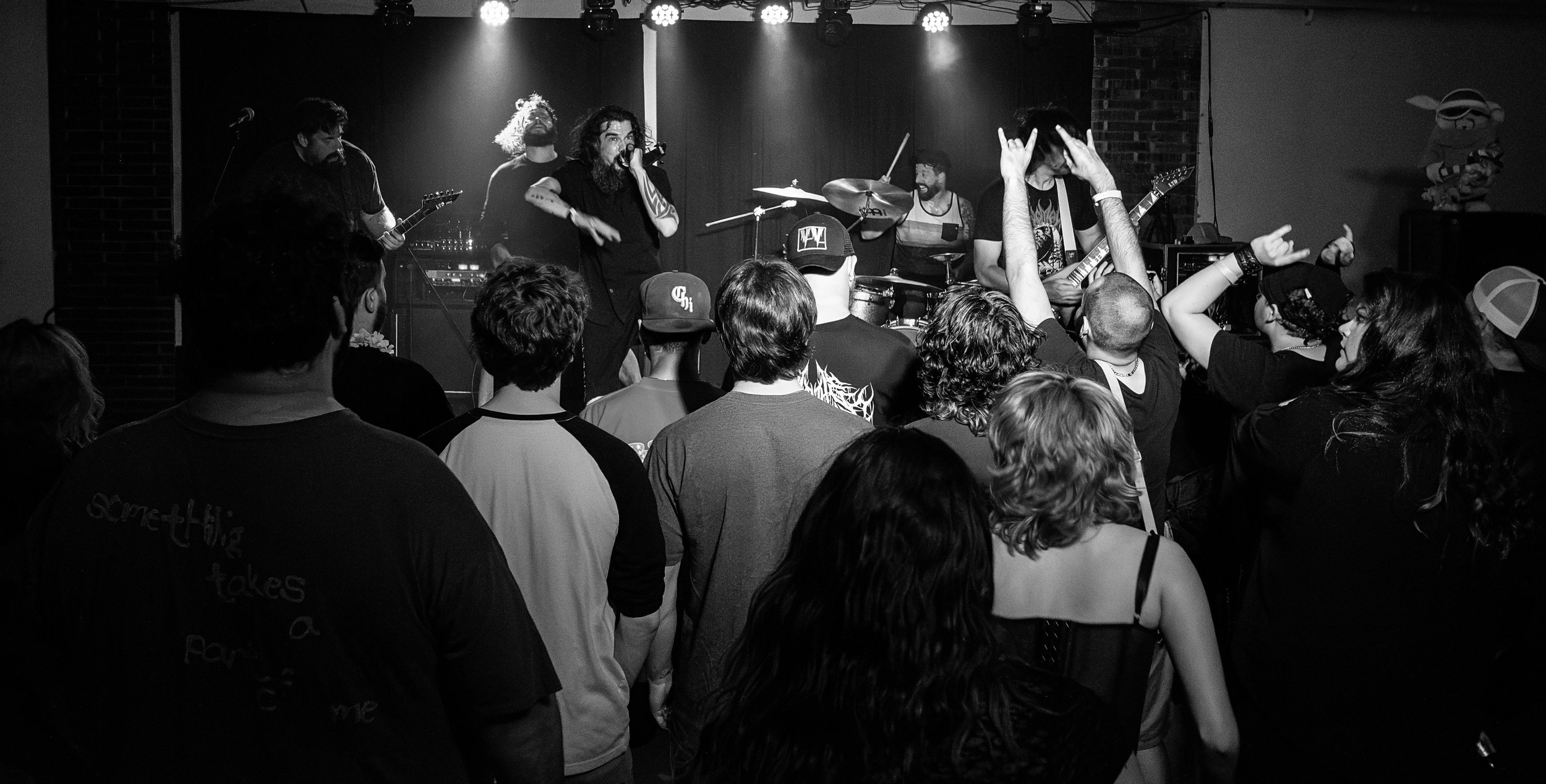 A black-and-white photo of a live music performance with a band on stage and an audience watching.