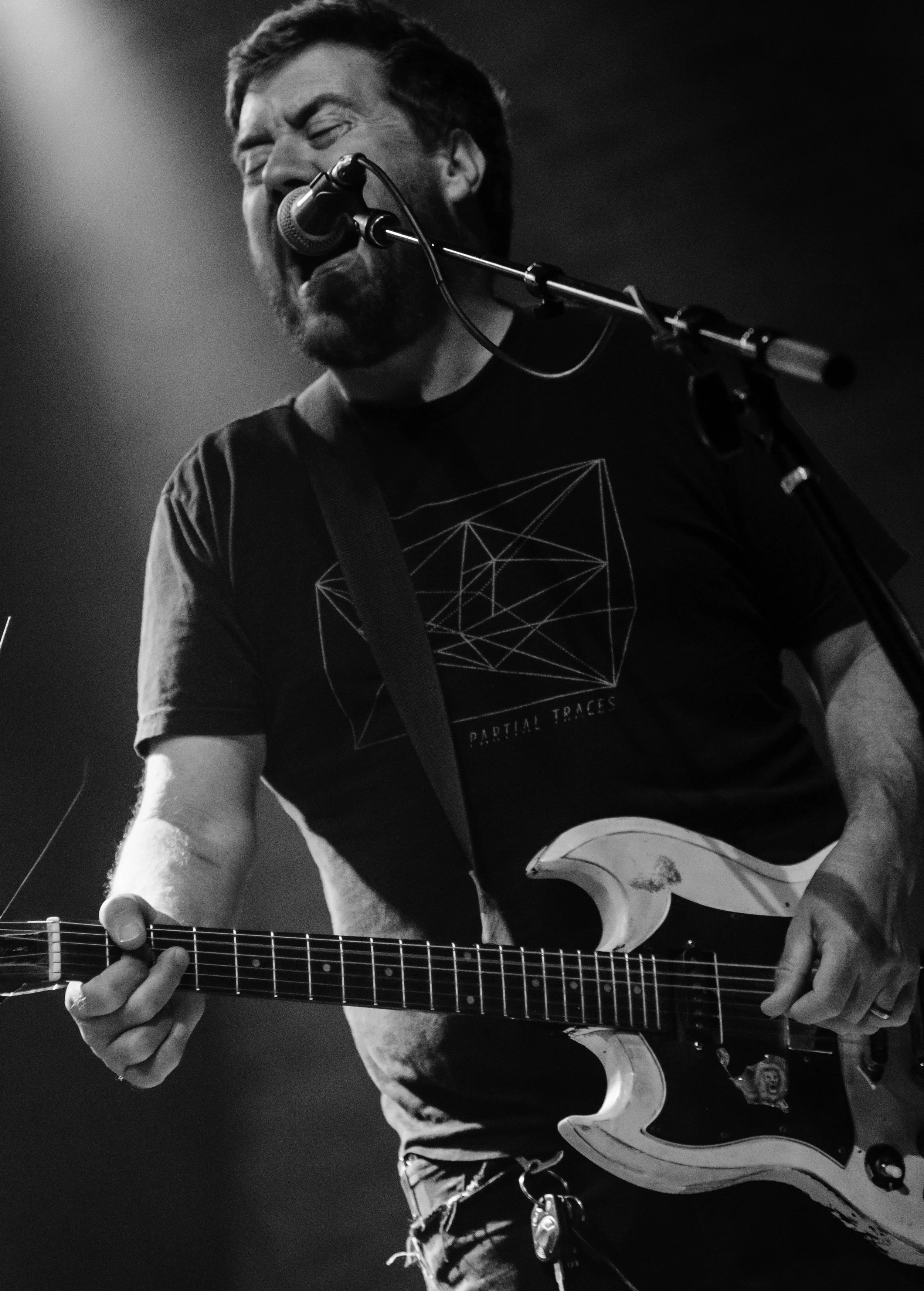 Black and white photo of a man singing into a microphone while playing an electric guitar.