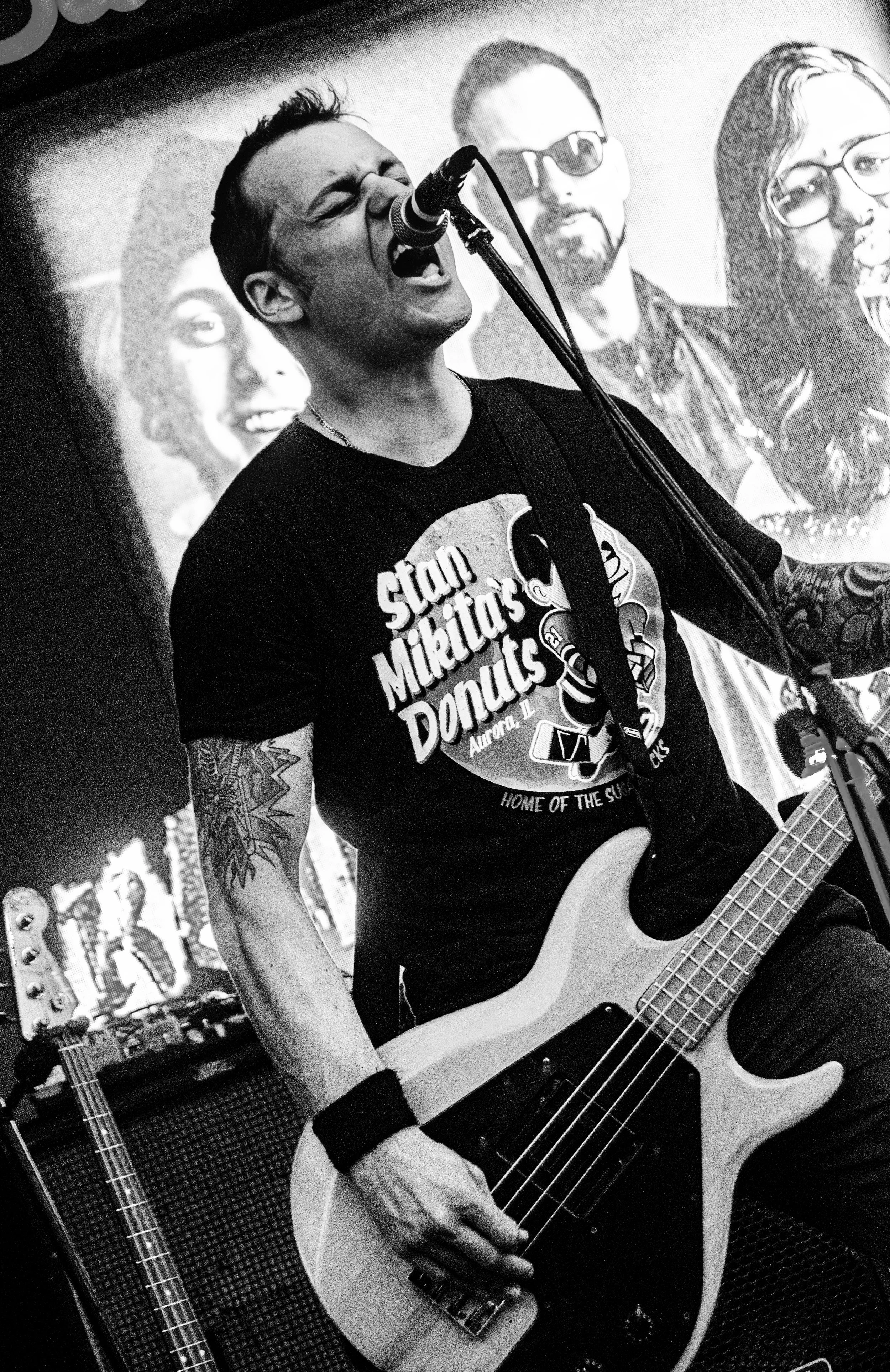 A man singing into a microphone while playing an acoustic guitar, with posters and musical equipment in the background.