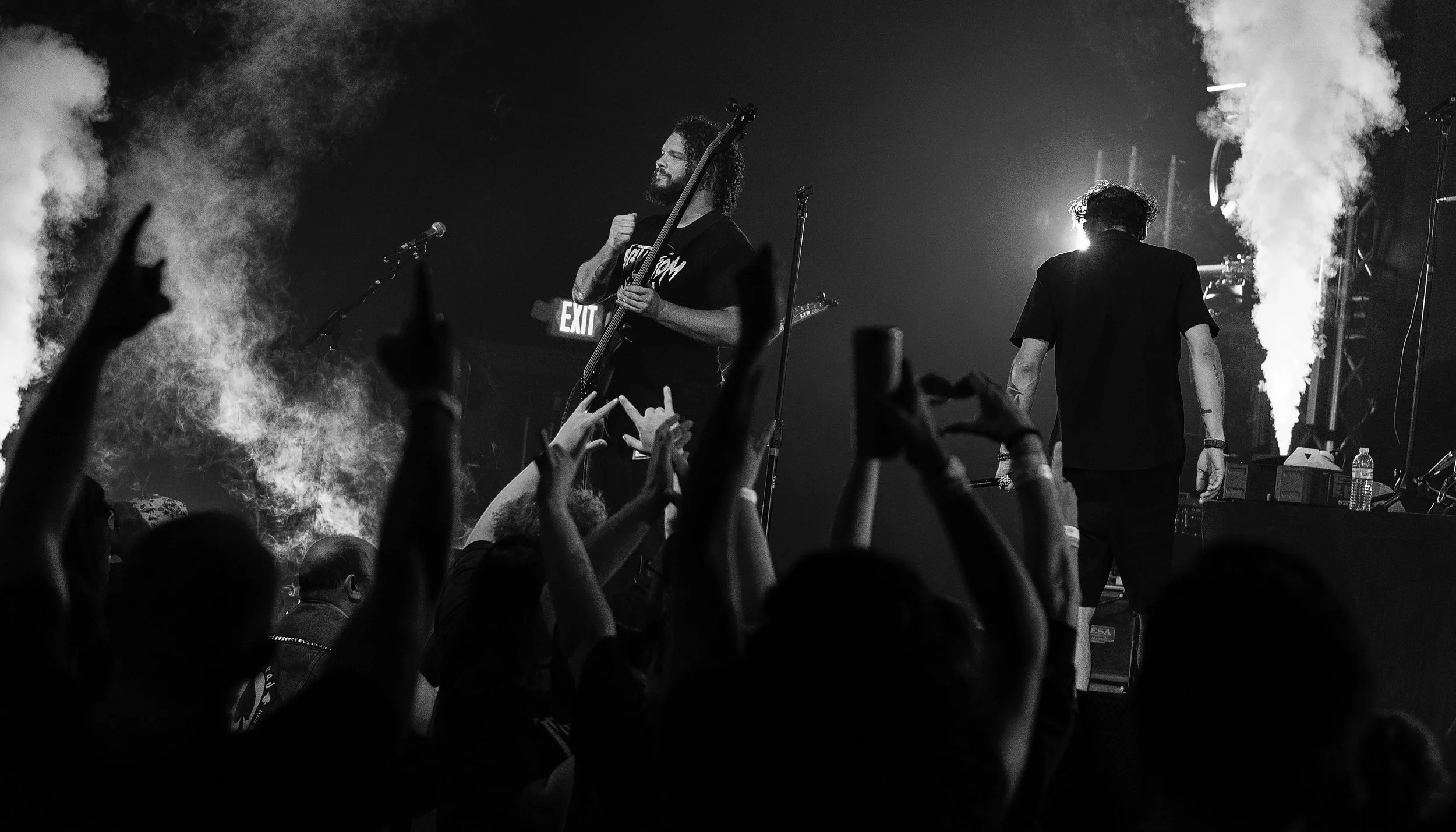 Black and white photo of a live concert with musicians on stage and an audience with hands raised.