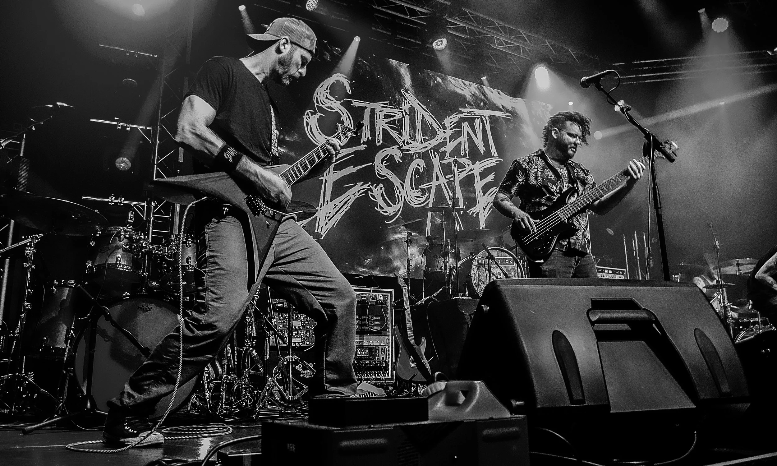 Two musicians playing electric guitars on stage during a concert, with a large illuminated sign reading 'Soriden Scar' in the background, black and white image, stage lighting effects.