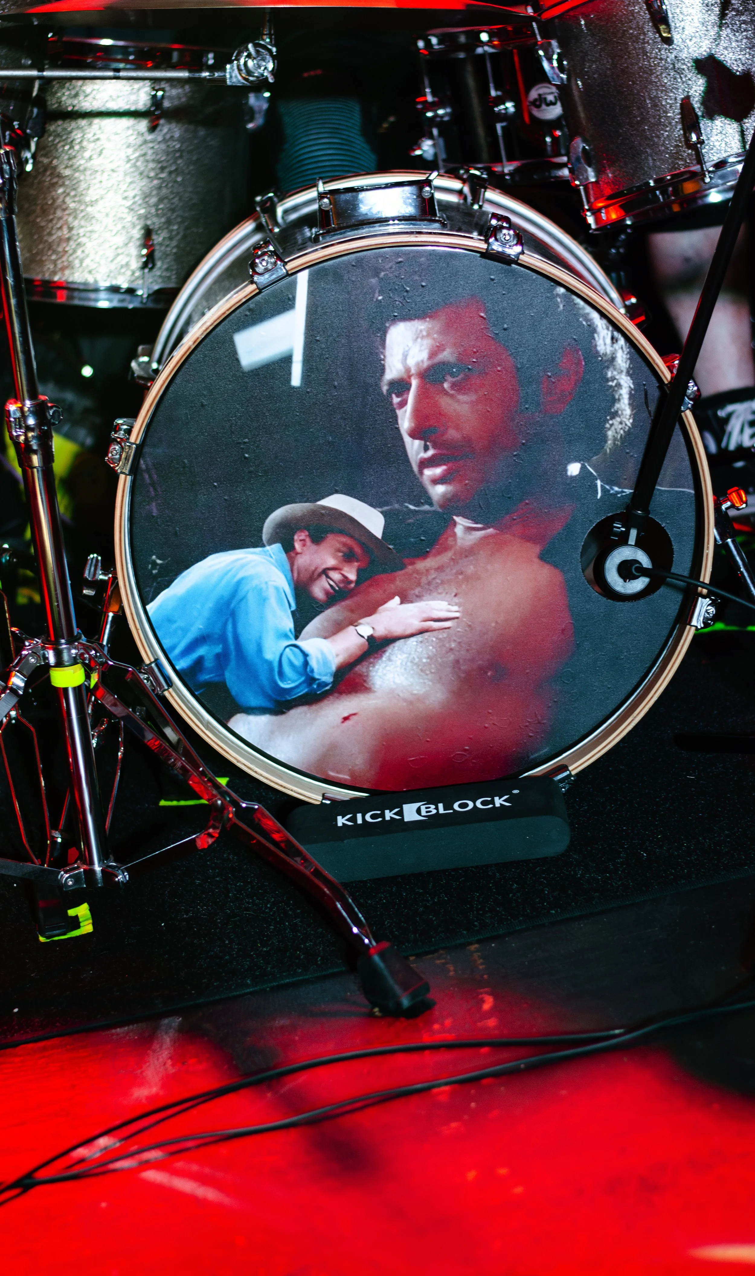 A drum set with a bass drum featuring a graffiti-style image of a man with dark hair and a serious expression, and a woman wearing a hat seemingly having an intimate moment with him.