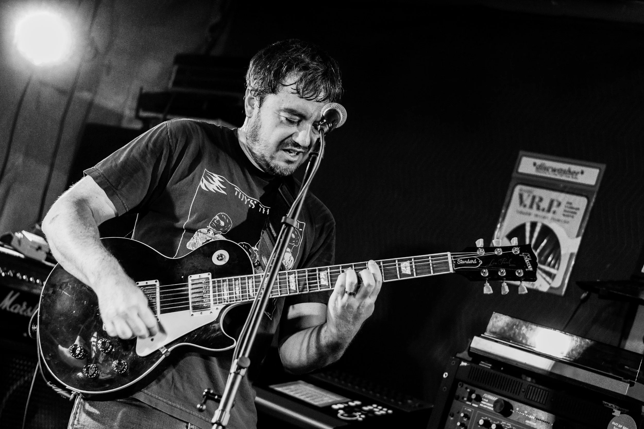 A man playing an electric guitar in a music studio, with musical equipment and a Marshall amplifier in the background.