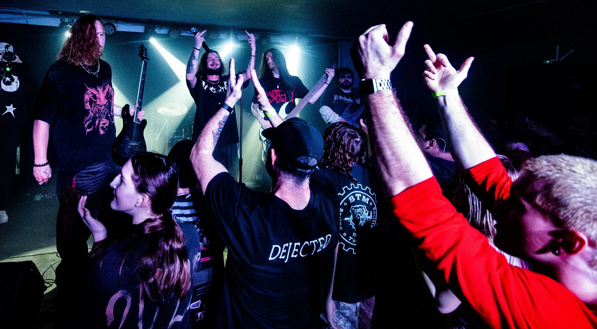A live band performing on stage with an audience raising their hands and enjoying the concert.