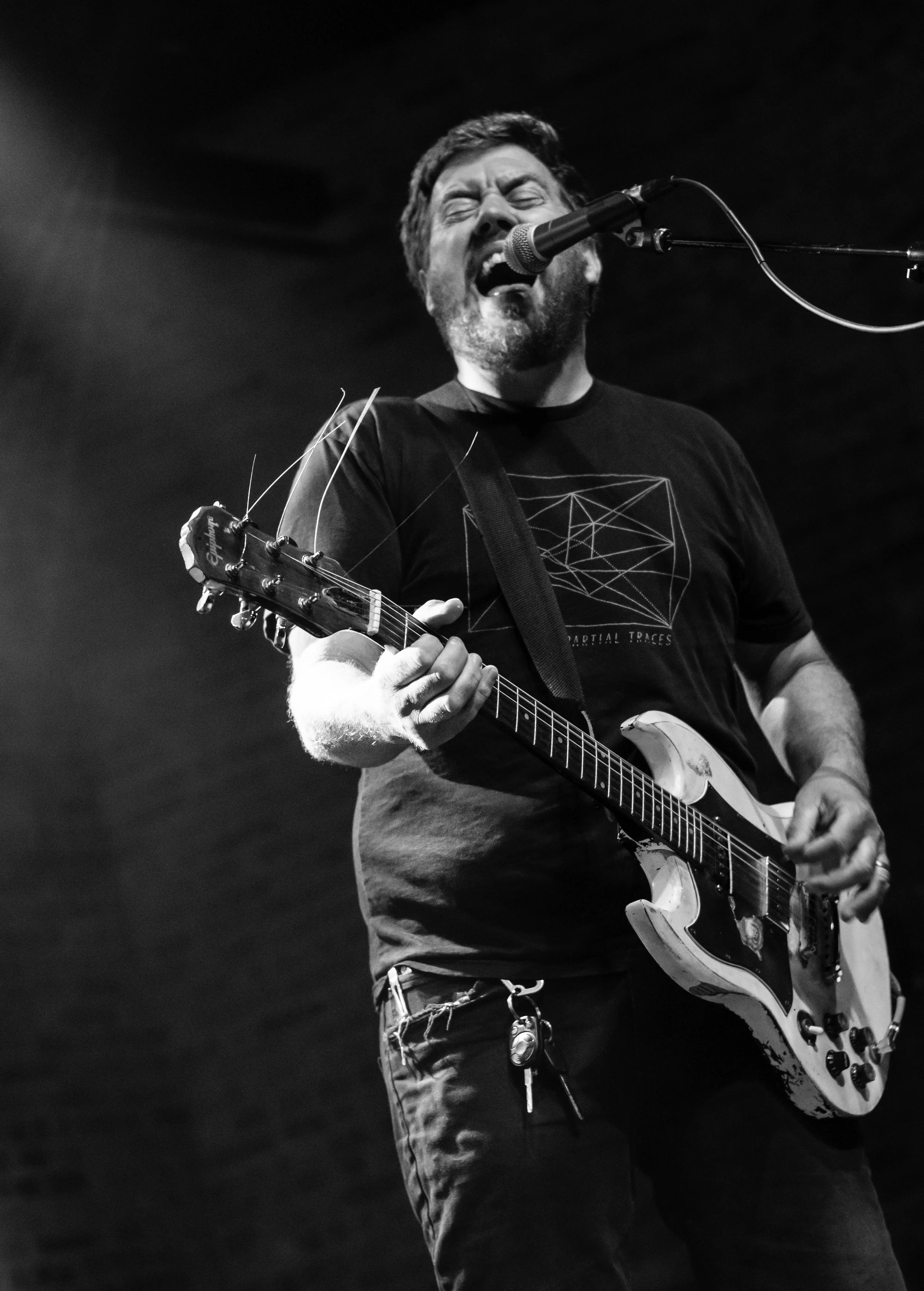 Black and white photo of a man passionately singing into a microphone while playing an electric guitar.