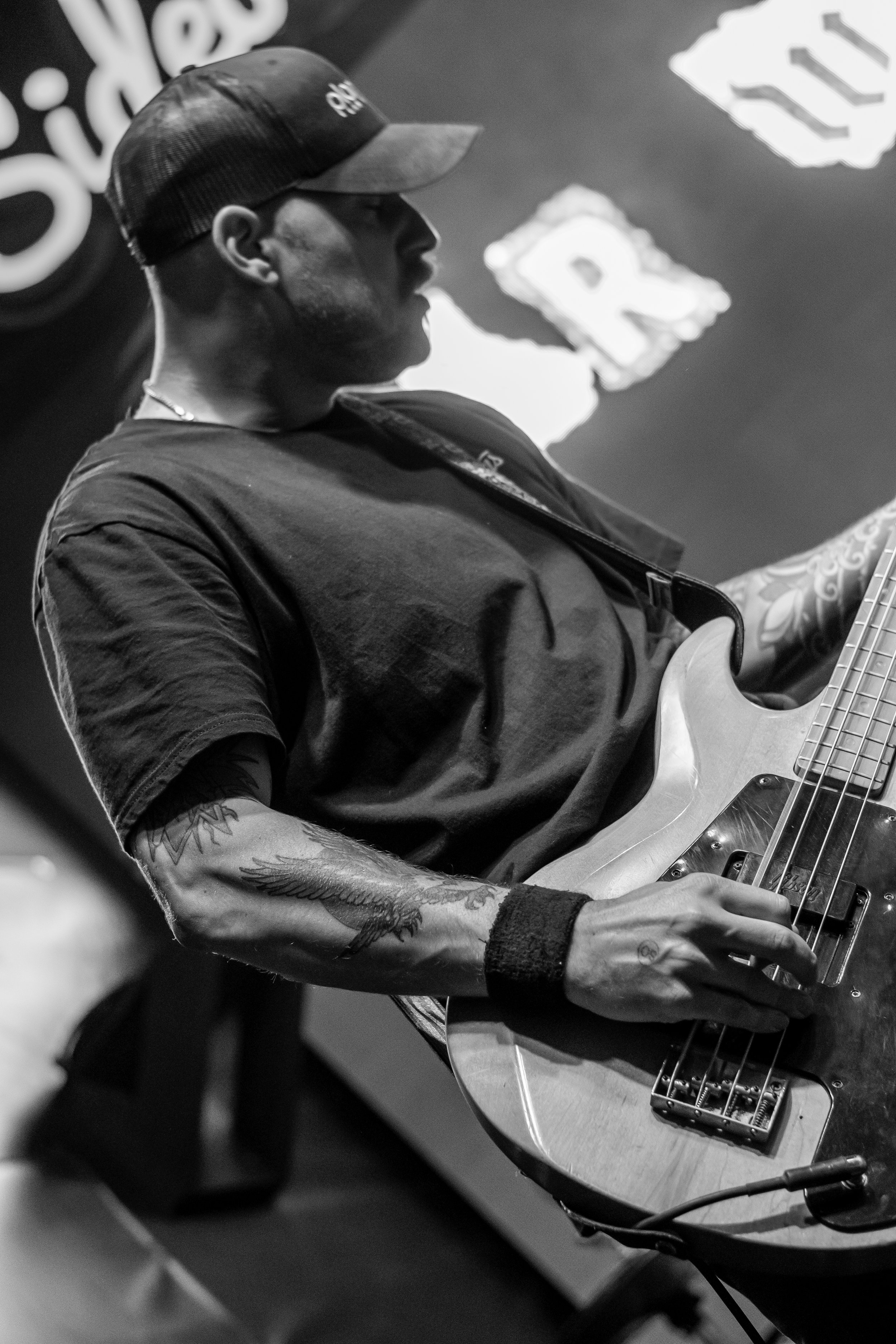 A person with tattoos on their arm, wearing a cap and a t-shirt, is playing an electric guitar. The image is in black and white.