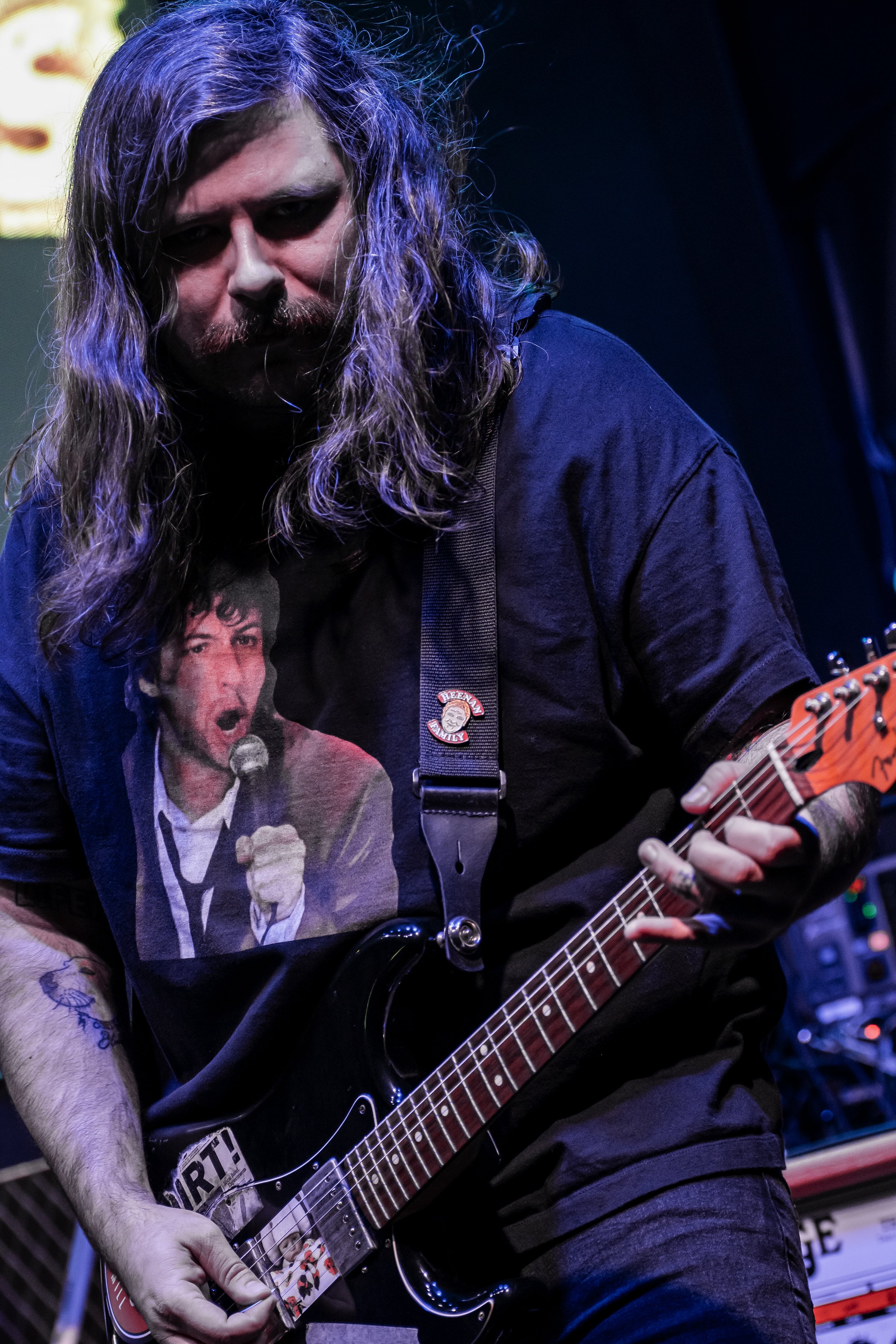 Close-up of a person with long wavy hair playing an electric guitar, wearing a graphic T-shirt featuring a man singing into a microphone.