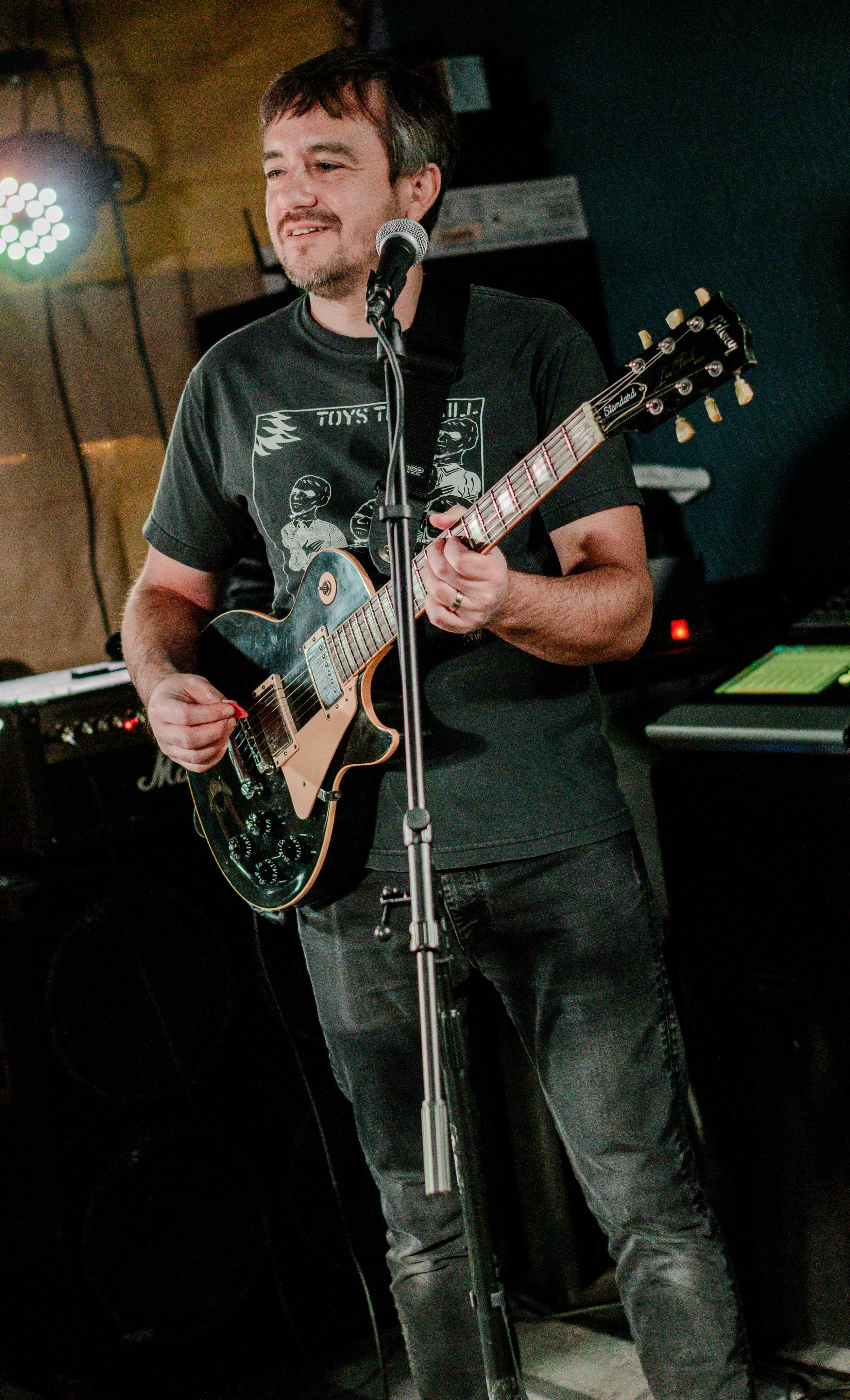 Man playing an electric guitar singing into a microphone during a performance in a dimly lit room.