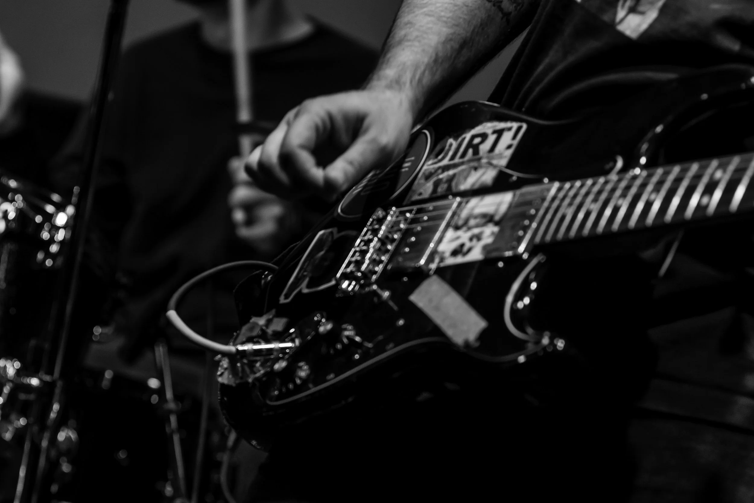 Black and white photo of a person playing an electric guitar, focusing on the hand and guitar neck.