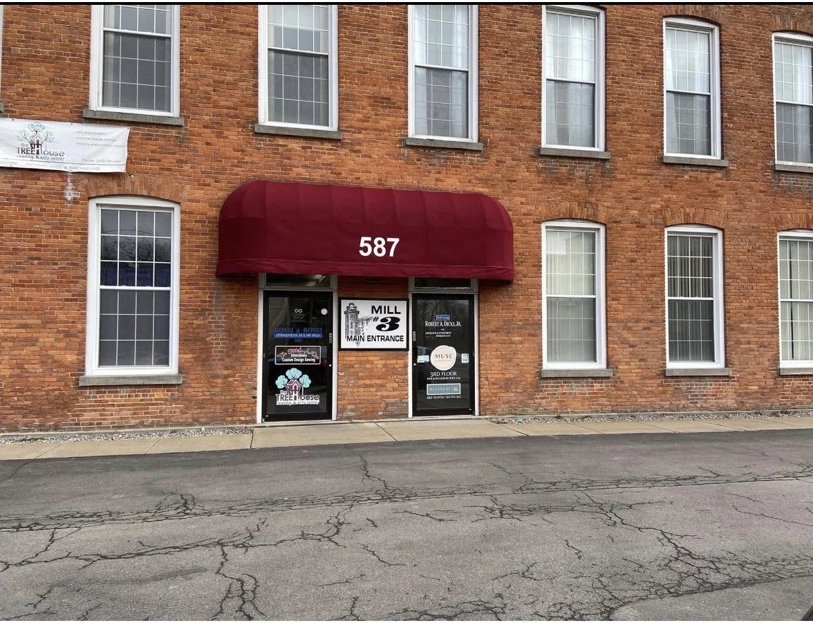 Brick building with six windows, entrance with a maroon awning, and various signs including 'Mill 3. Main Entrance' and business advertisements.