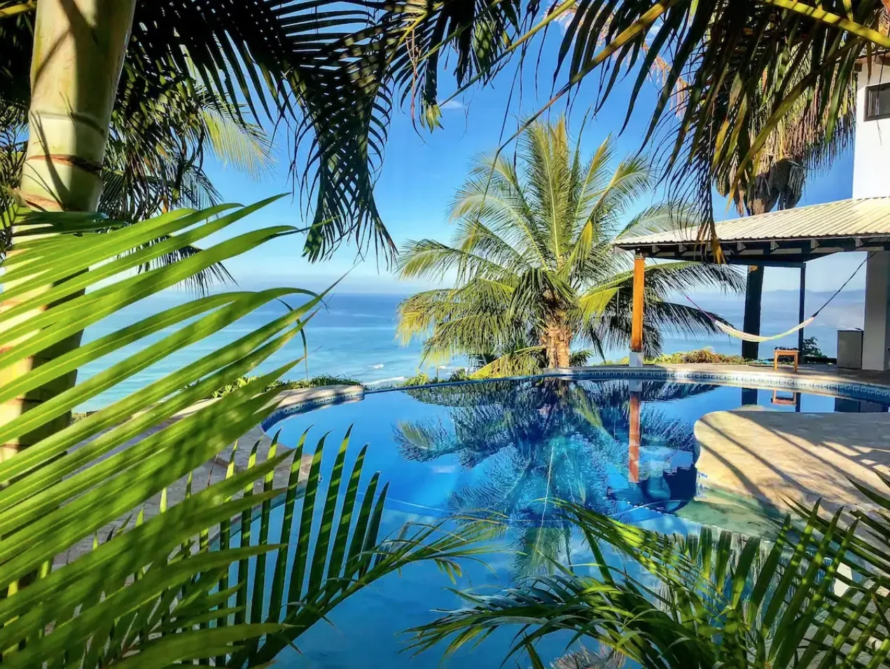 Infinity pool with palm trees, hammock and sweeping ocean view — Mal País, Costa Rica Airbnb vacation rental.