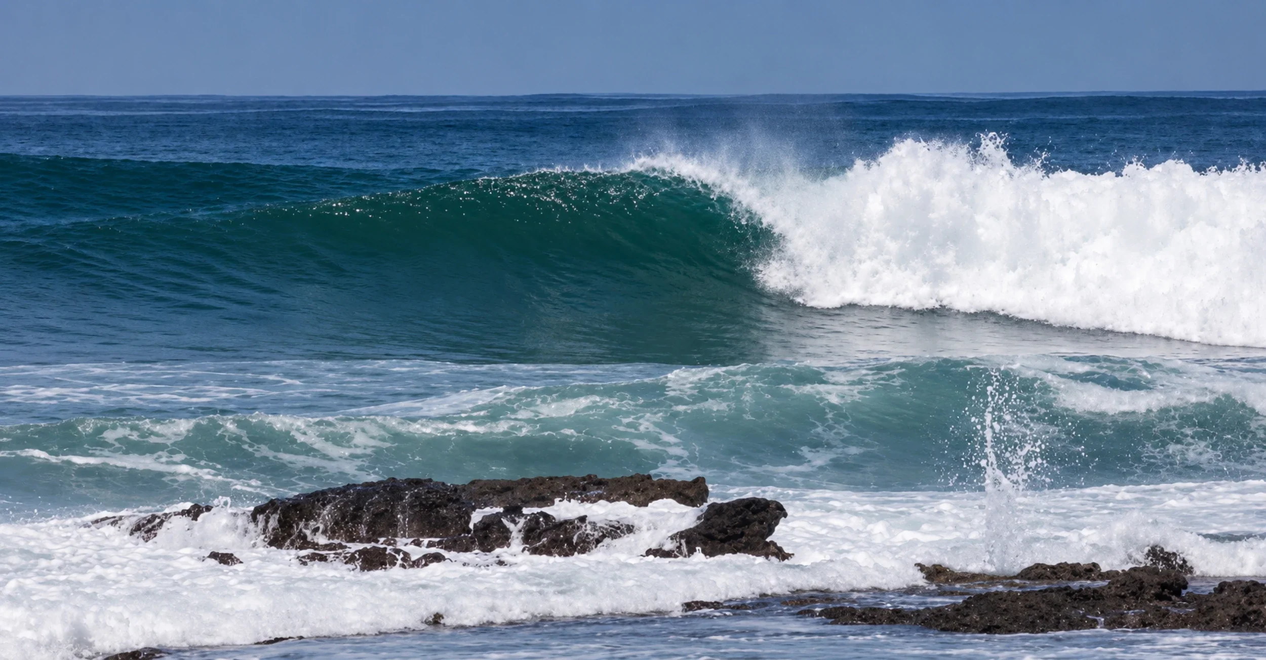 Powerful wave breaking behind coastal rocks at Suck Rock in Santa Teresa, Costa Rica.