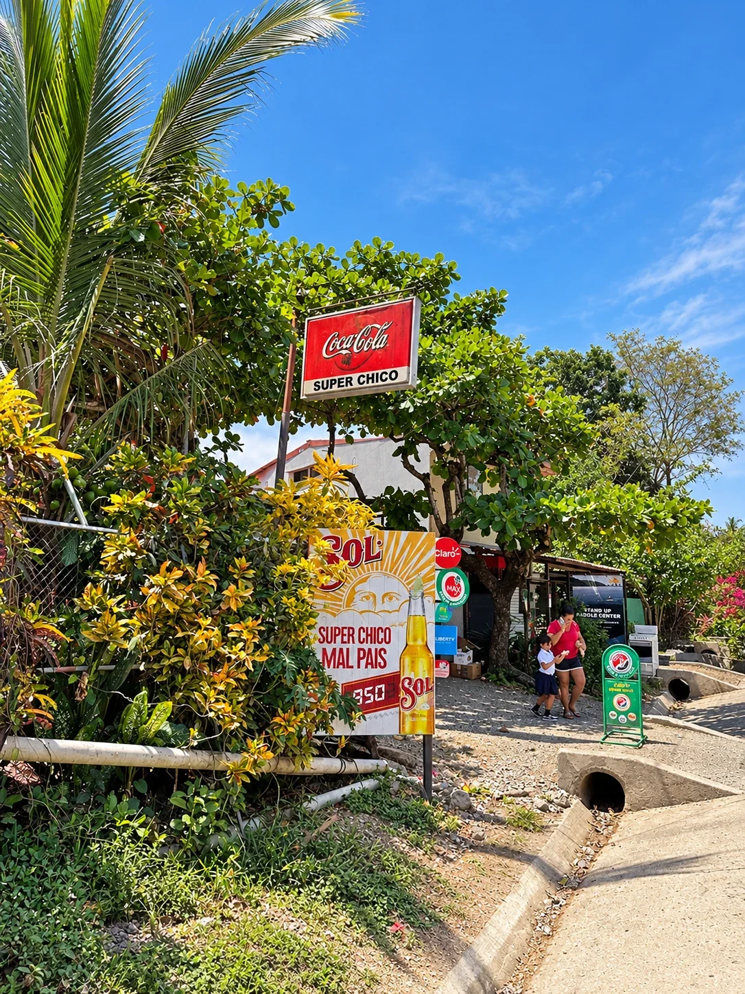 Super Chico grocery store entrance and roadside signs surrounded by tropical greenery in Mal País, Costa Rica.