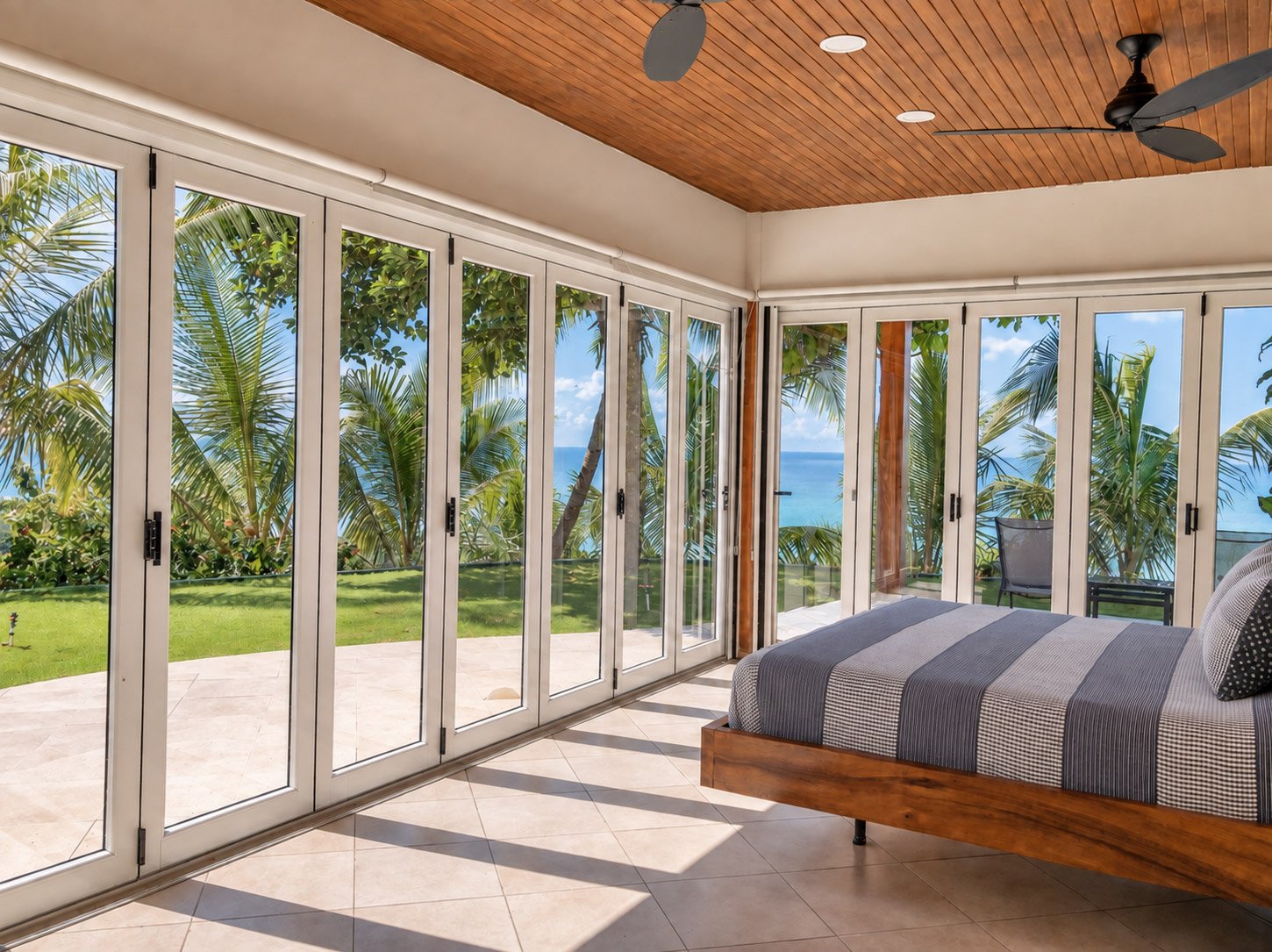 Casa Rita bedroom with wraparound glass doors overlooking a palm-lined terrace and the Pacific Ocean in Mal País, Costa Rica.