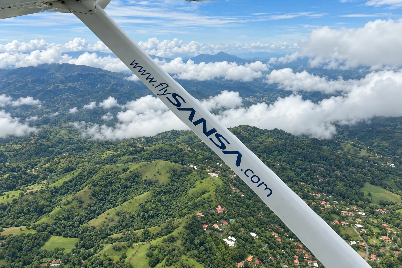 View from a SANSA flight over Costa Rica’s green hills and clouds, with the aircraft’s wing strut in the foreground.