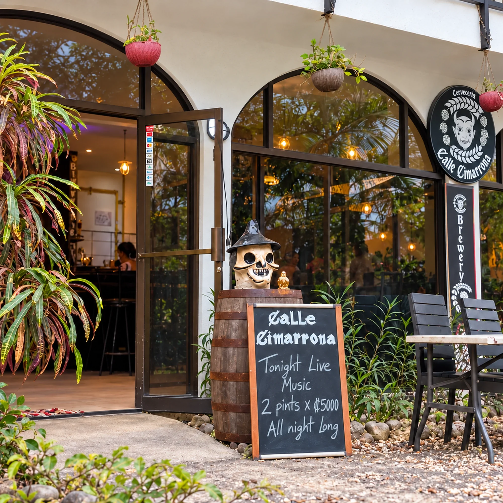 Calle Cimarrona Brewery entrance in Mal País, Costa Rica, with tropical plants, outdoor seating and a chalkboard advertising live music.