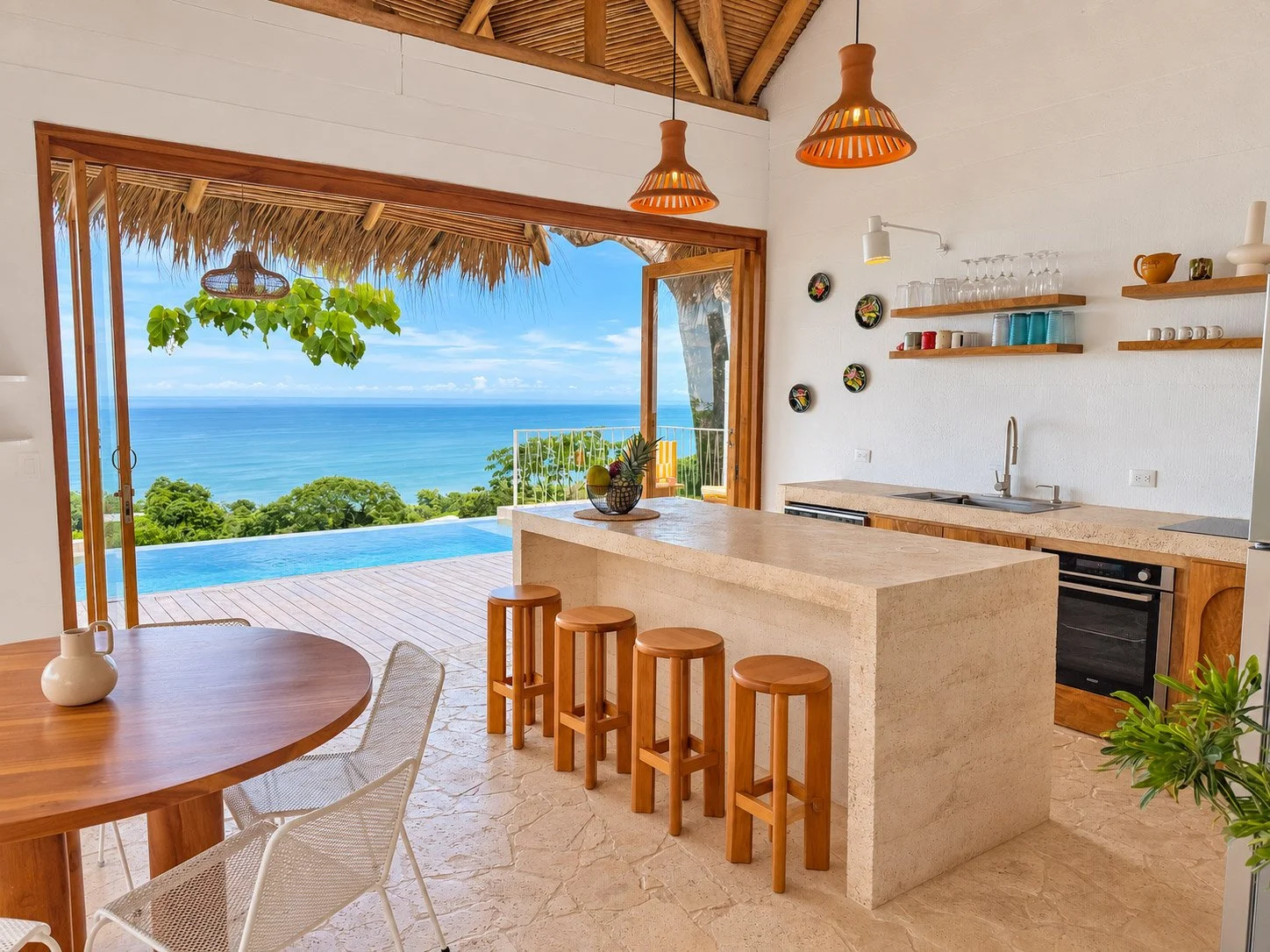 Casa Selva’s open kitchen with a stone island and wooden stools, overlooking the infinity pool and Pacific Ocean in Mal País, Costa Rica.