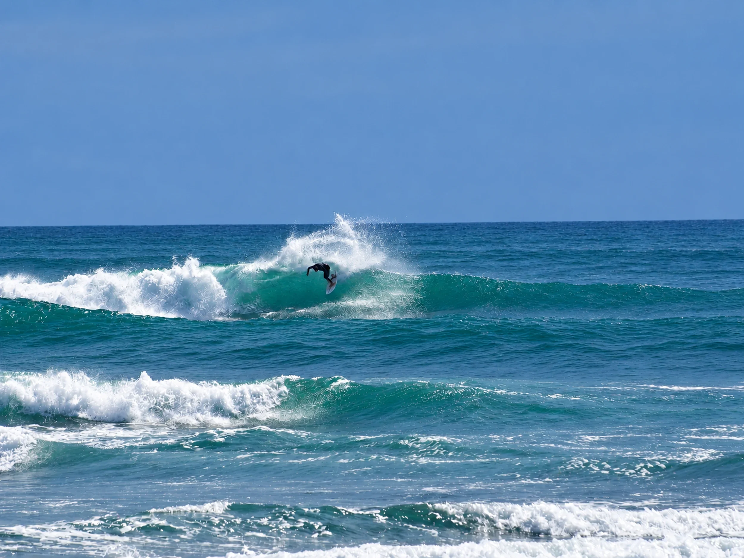 Surfer carving a turquoise wave and throwing spray at an outer reef in Mal País, Costa Rica.