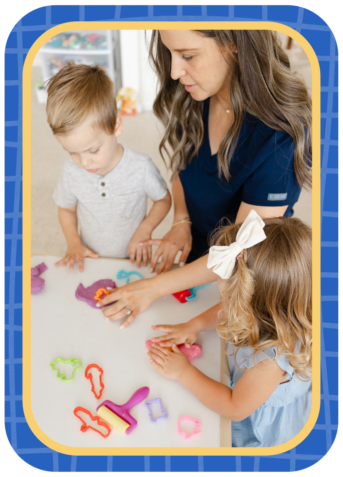 A woman and two young children playing with colorful playdough and cookie cutters at a table in a bright room.