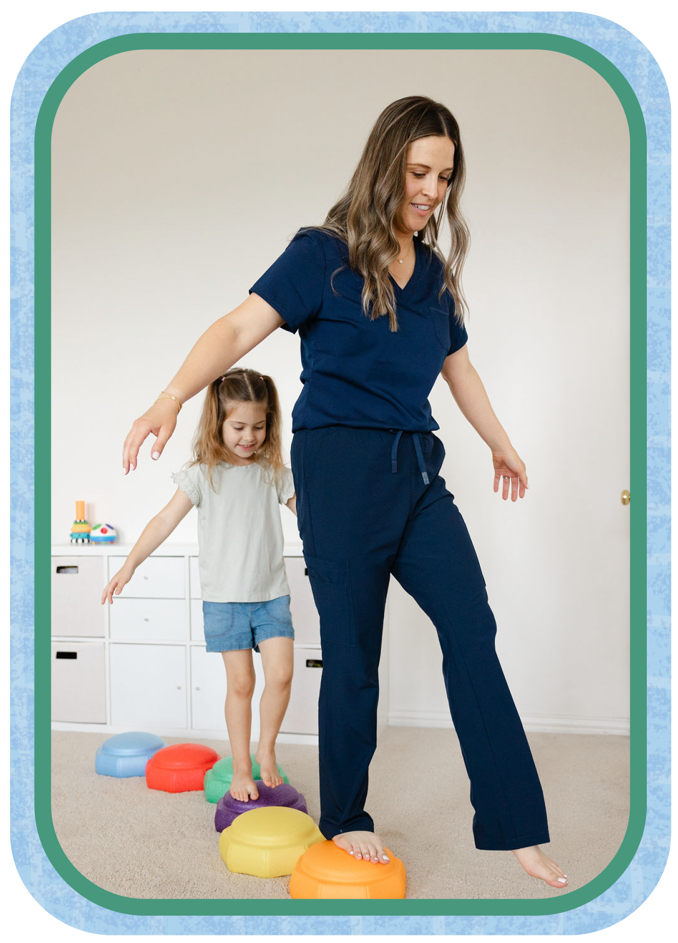 A woman and a girl walking in a line, stepping on colorful stepping stones inside a room with a white wall and a storage unit in the background.