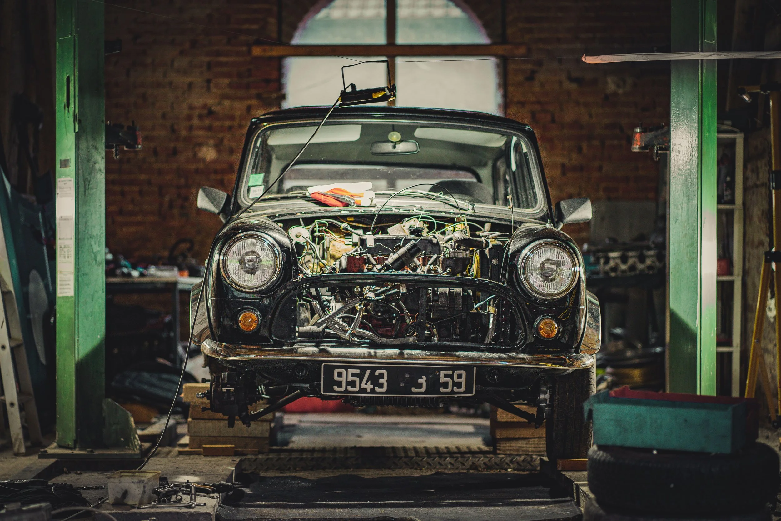 An old car on a lift in a garage being repaired, with tools and parts around.