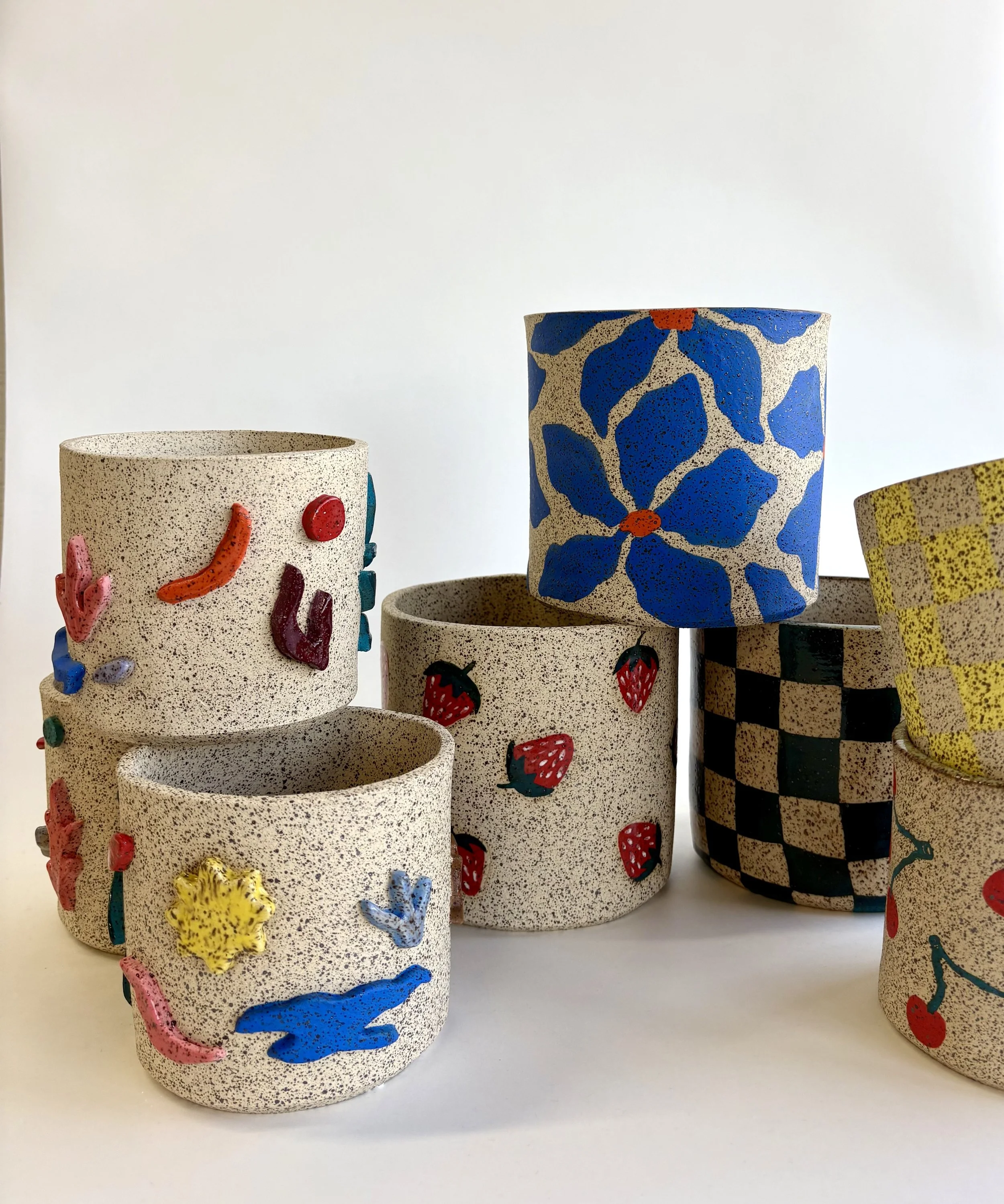 Collection of textured ceramic cups with colorful, raised floral and animal designs on a white background.
