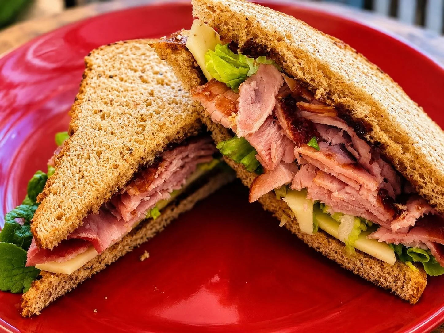 Two halves of a multigrain sandwich with sliced turkey, lettuce, cheese, and bacon on a red plate.