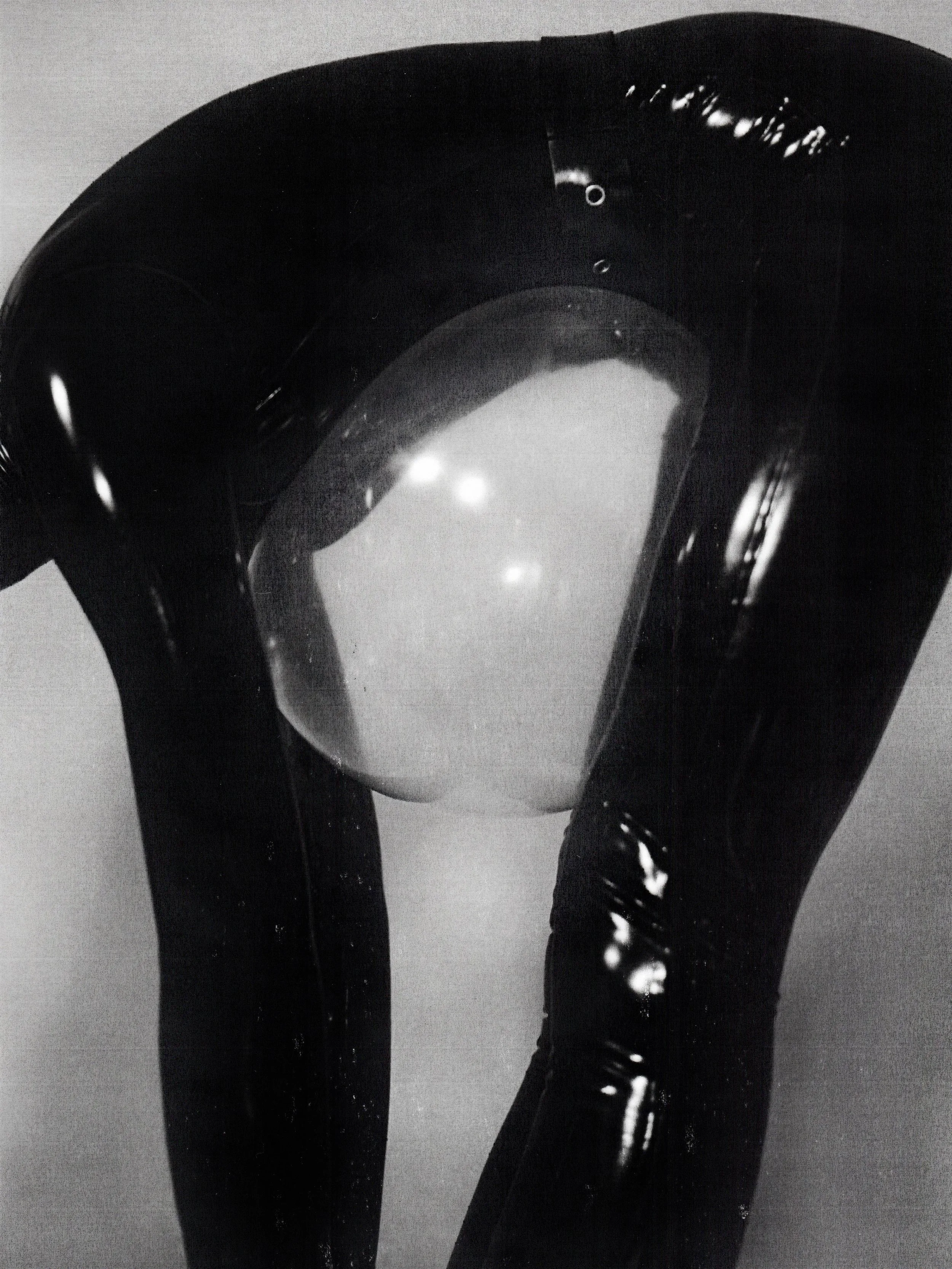 Close-up of black shiny latex or leather pants worn by a person, with reflections on the material.