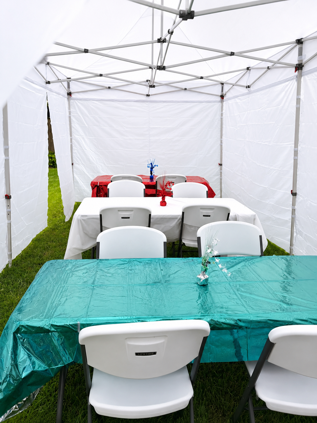 Party tent with tables decorated for a celebration, including red, white, and blue tablecloths and centerpieces on each table placed outdoors on grass.