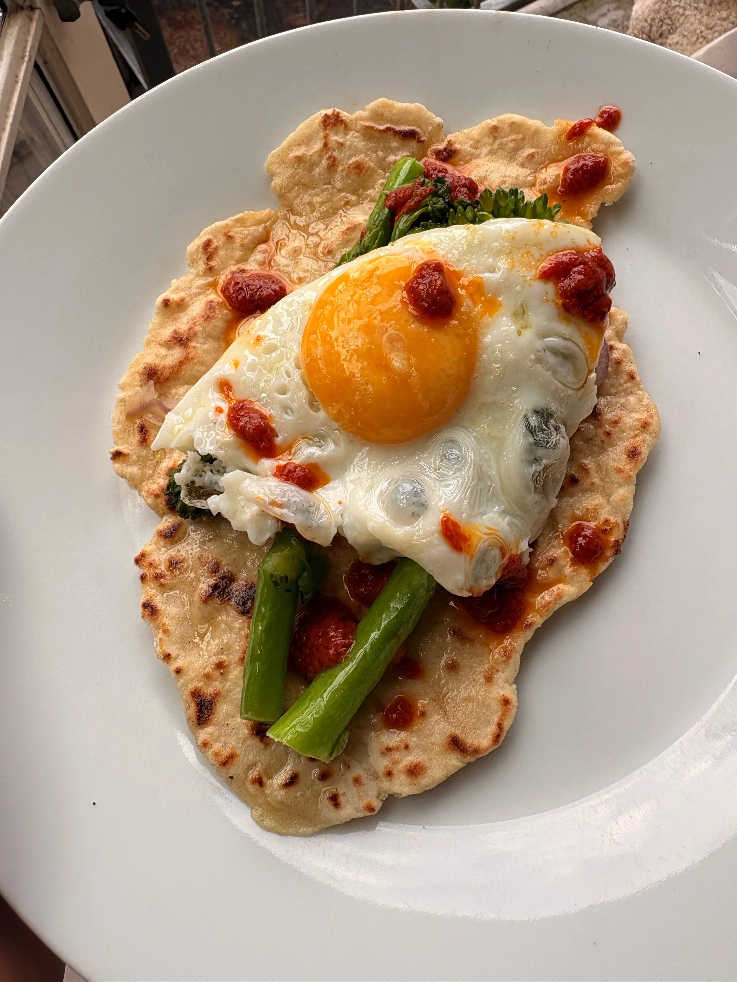 Homemade yoghurt flatbreads with (hiding) red onion, Tenderstem broccoli, fried eggs, good olive oil and harissa. 🥦 🍳
