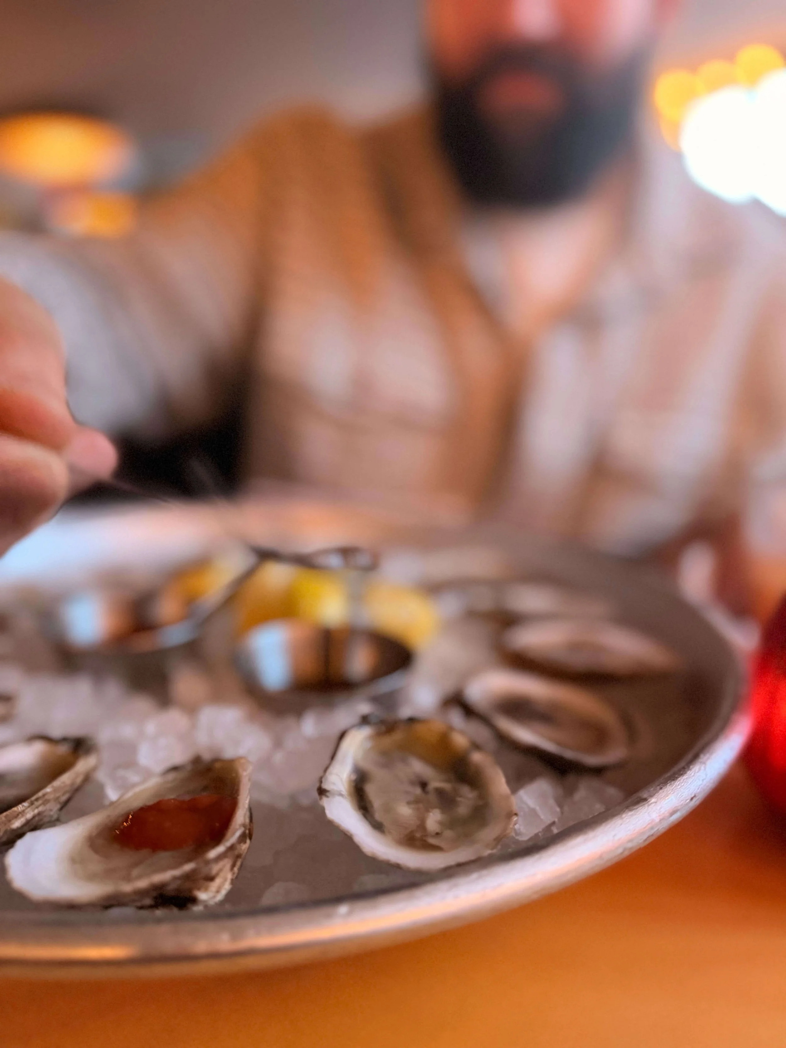 Close-up of a plate of cooked oysters on ice with some lemon wedges in the background.