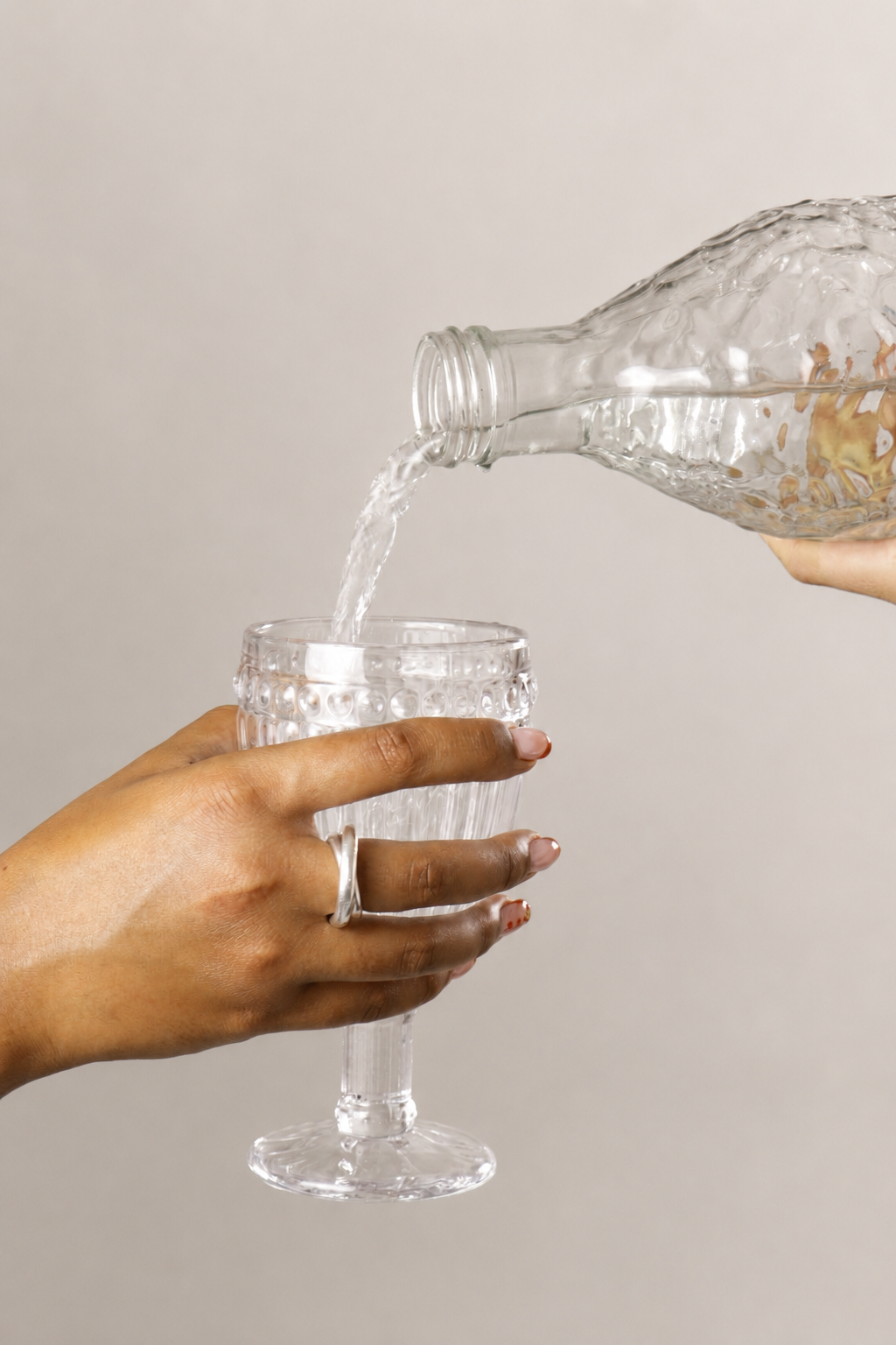 Une main tient un verre en cristal tandis qu'une autre main verse de l'eau d'une bouteille en verre.