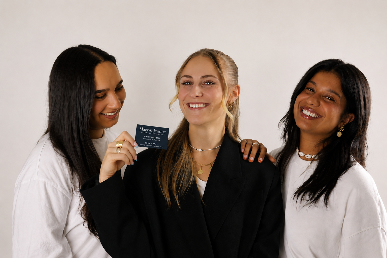 Trois femmes souriantes posent ensemble, une d'elles tient une carte de visite.