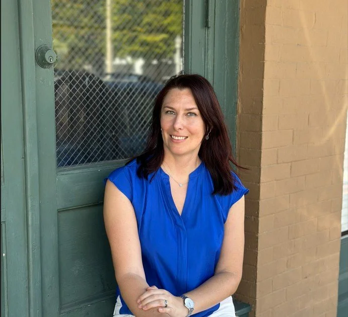 Natallia Khoshchynka Neuro Coach in blue shirt sitting by the door