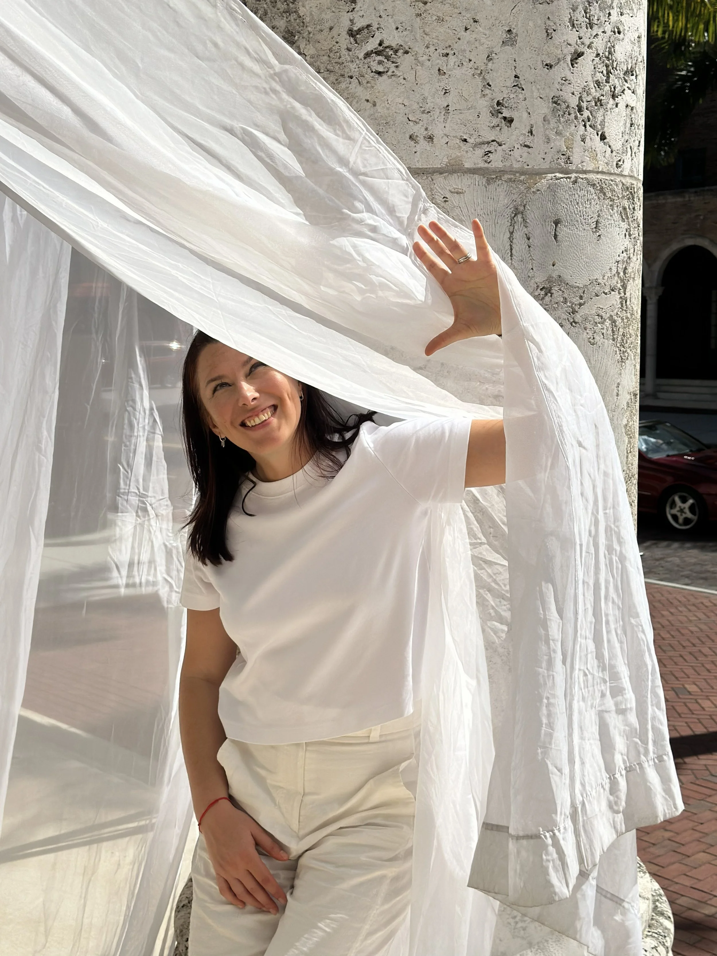 Natallia Khoshchynka Neuro Coach in while shirt and white pants standing by the column