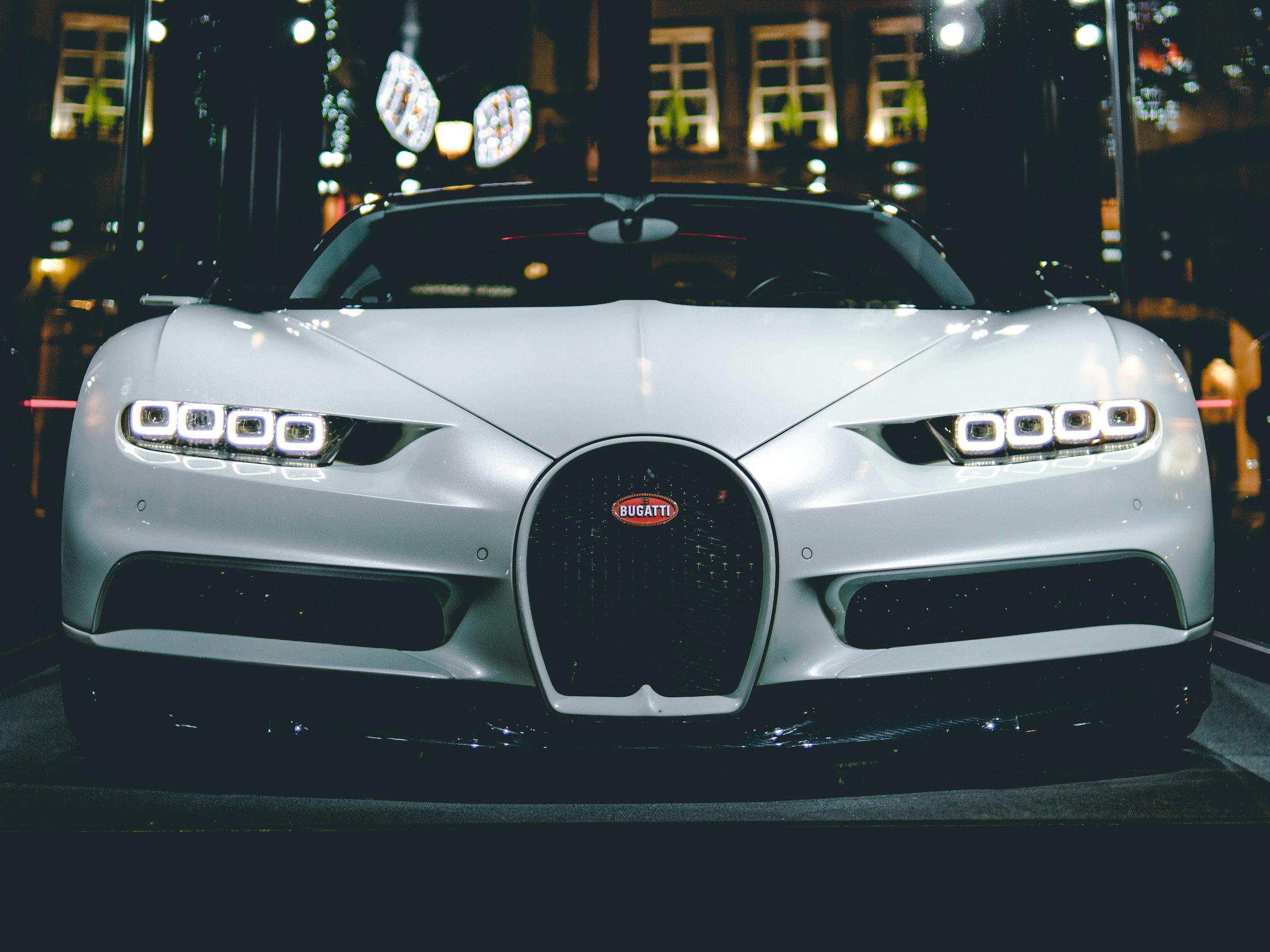 Front view of a white Bugatti sports car at night with illuminated city buildings in the background.