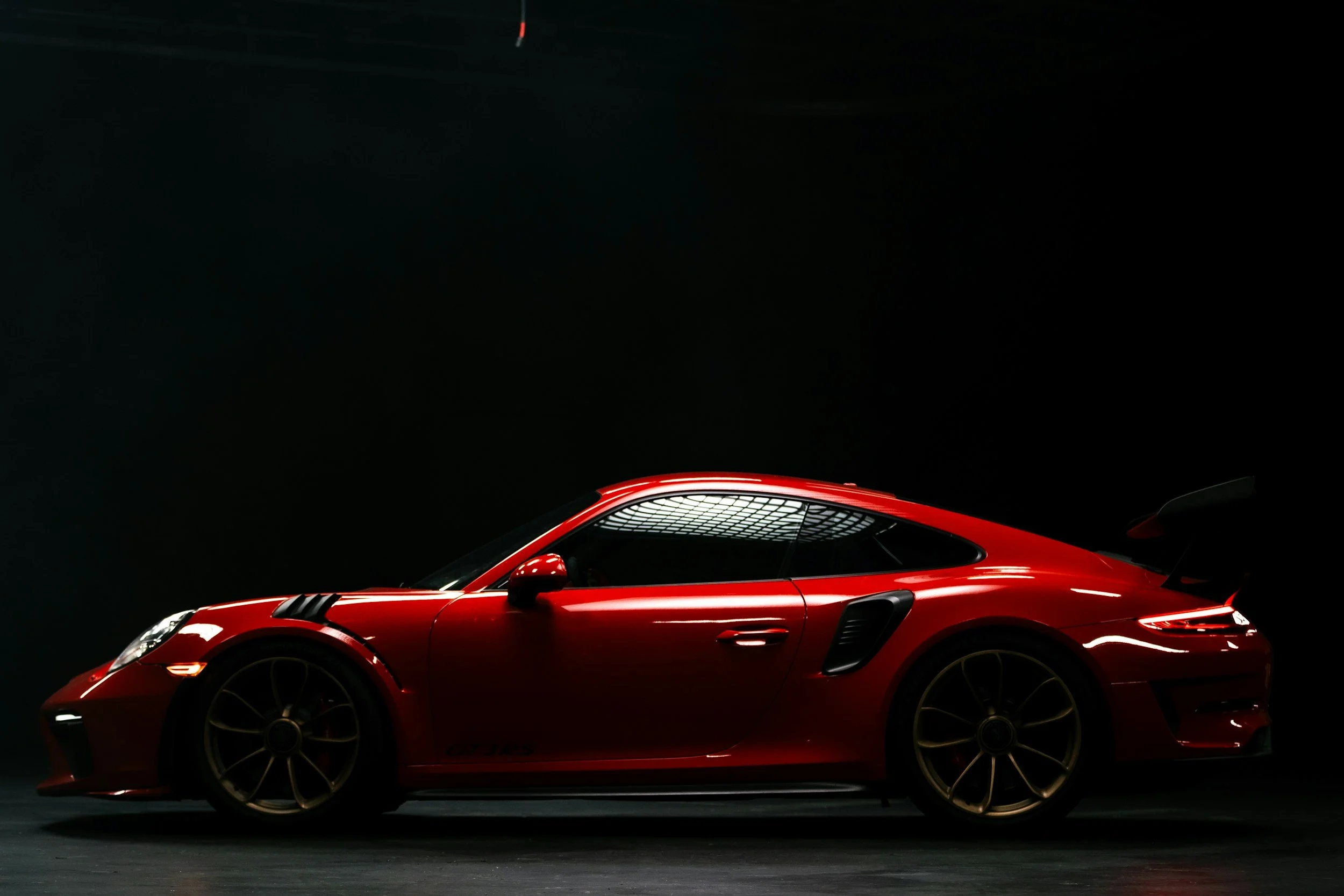 A sleek red sports car with black accents and large wheels, against a dark background.