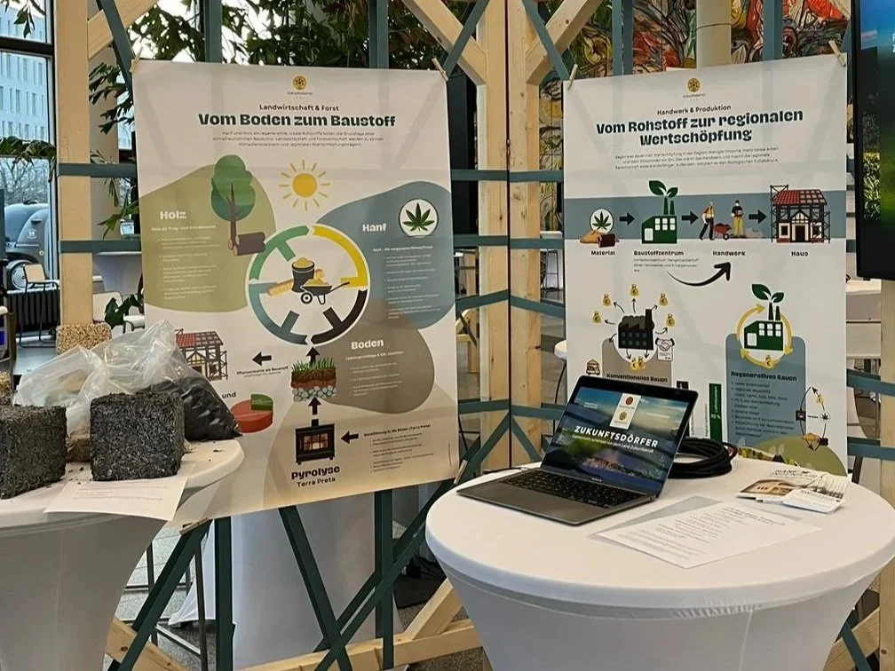 Infografiken über nachhaltige Baustoffe und regionale Wertschöpfung, ein Laptop und Materialien auf einer weißen runden Tafel.