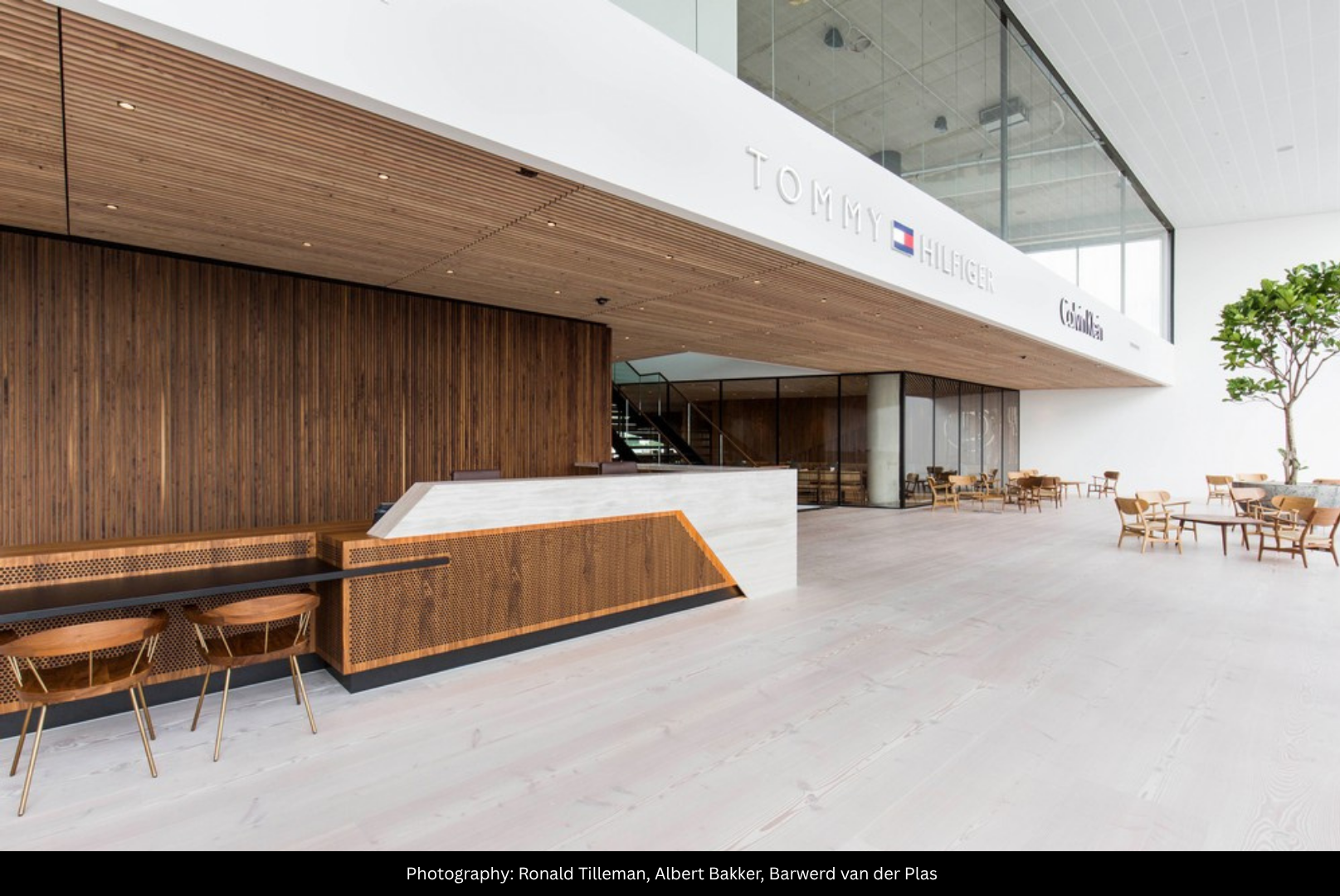 Modern hotel lobby with a reception desk, wooden accents, and a seating area with wooden chairs and tables, large windows, and a high ceiling.