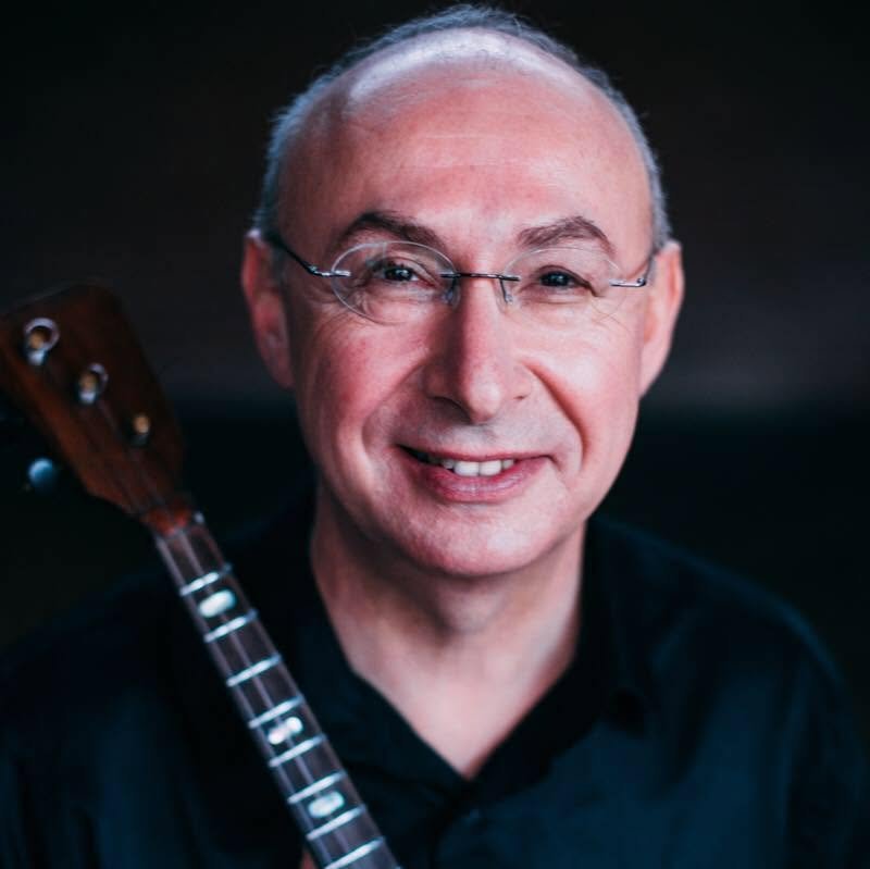 Ein lächelnder Mann mit Brille, der eine Balalaika trägt.