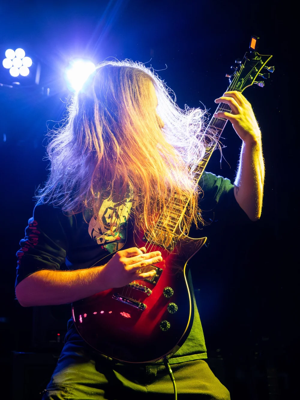 Electric guitarist performing under bright stage backlighting.