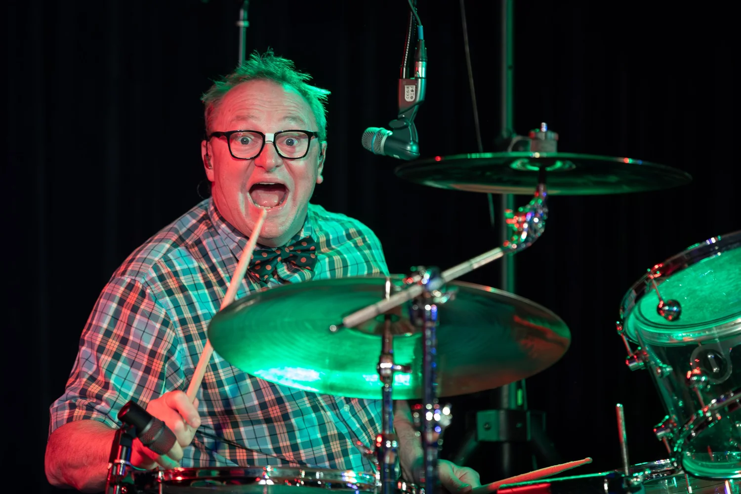 Live music drummer performing under colorful concert stage lighting.
