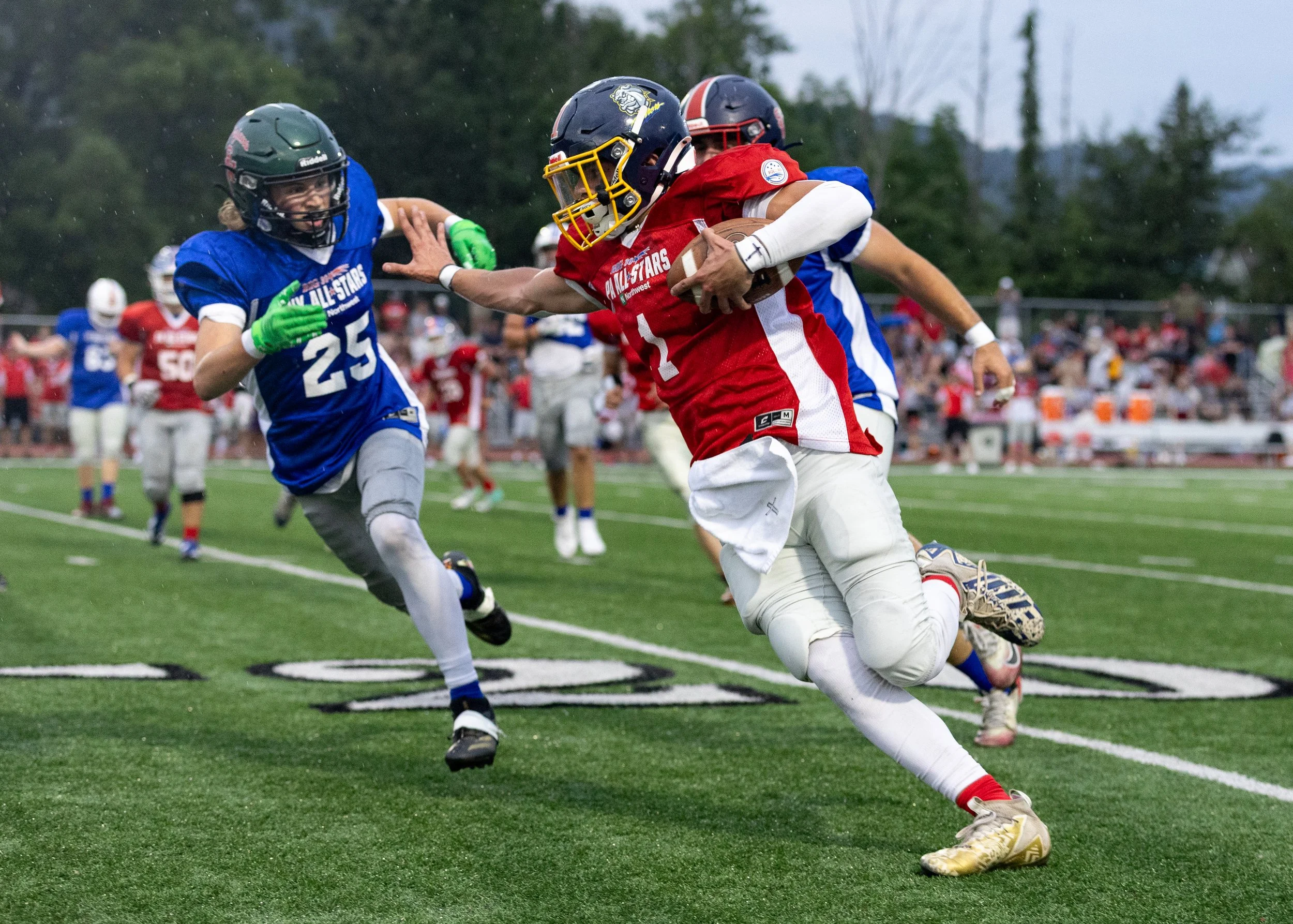 Football player in red carries the ball while a blue-uniformed defender makes a tackle at the Big 30 All-Star Charities Classic.
